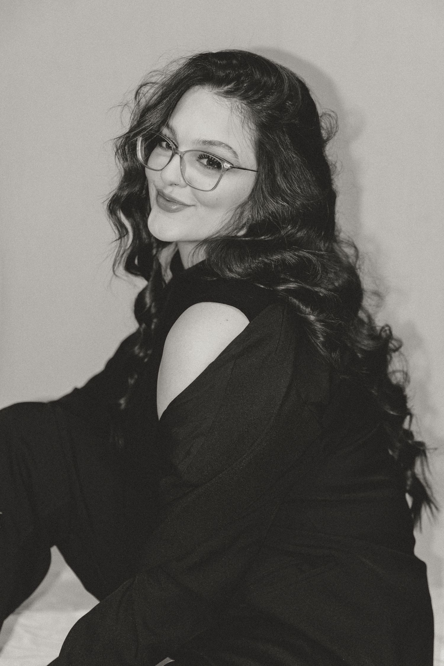 A series of black and white photos showing a person with dark curly hair and glasses wearing a black sweater in different poses.
