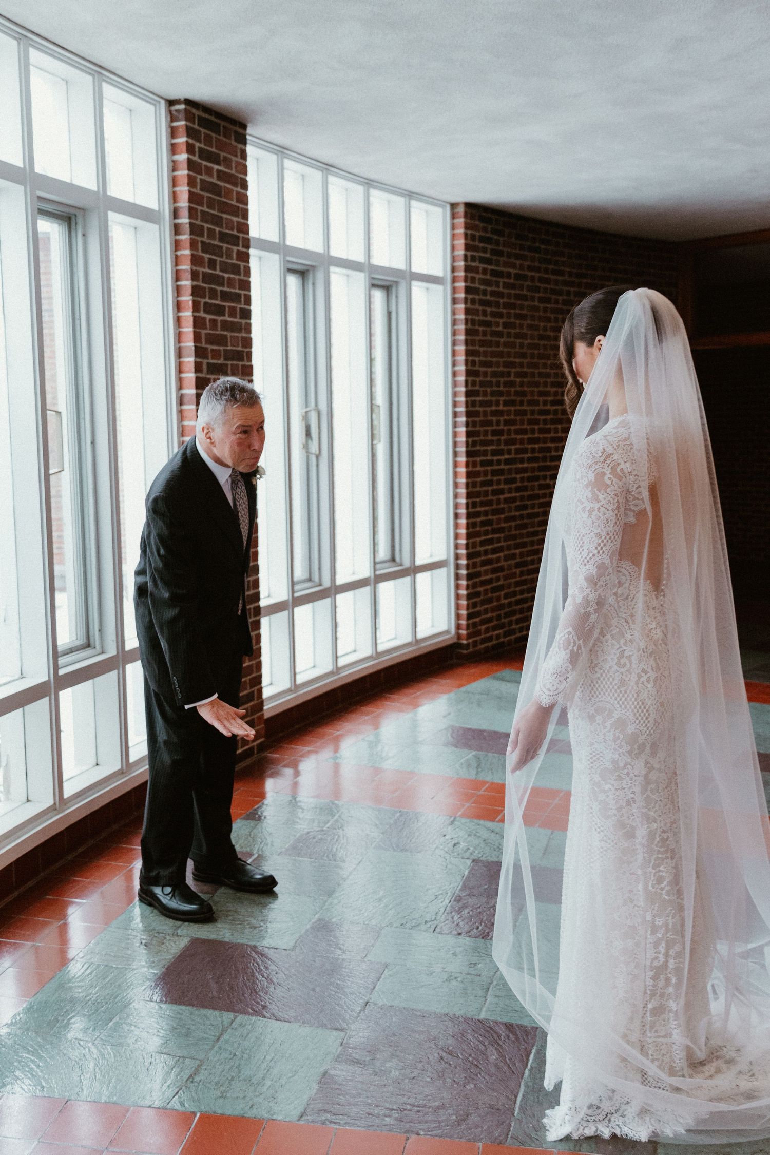 A wedding moment captured in a brick-walled room with large windows and checkerboard floor.