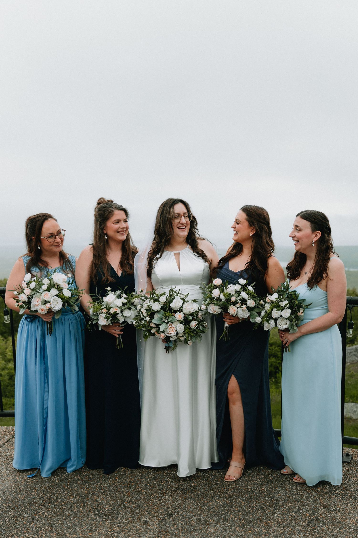 Bridesmaids in coordinating blue and navy dresses holding white floral bouquets.