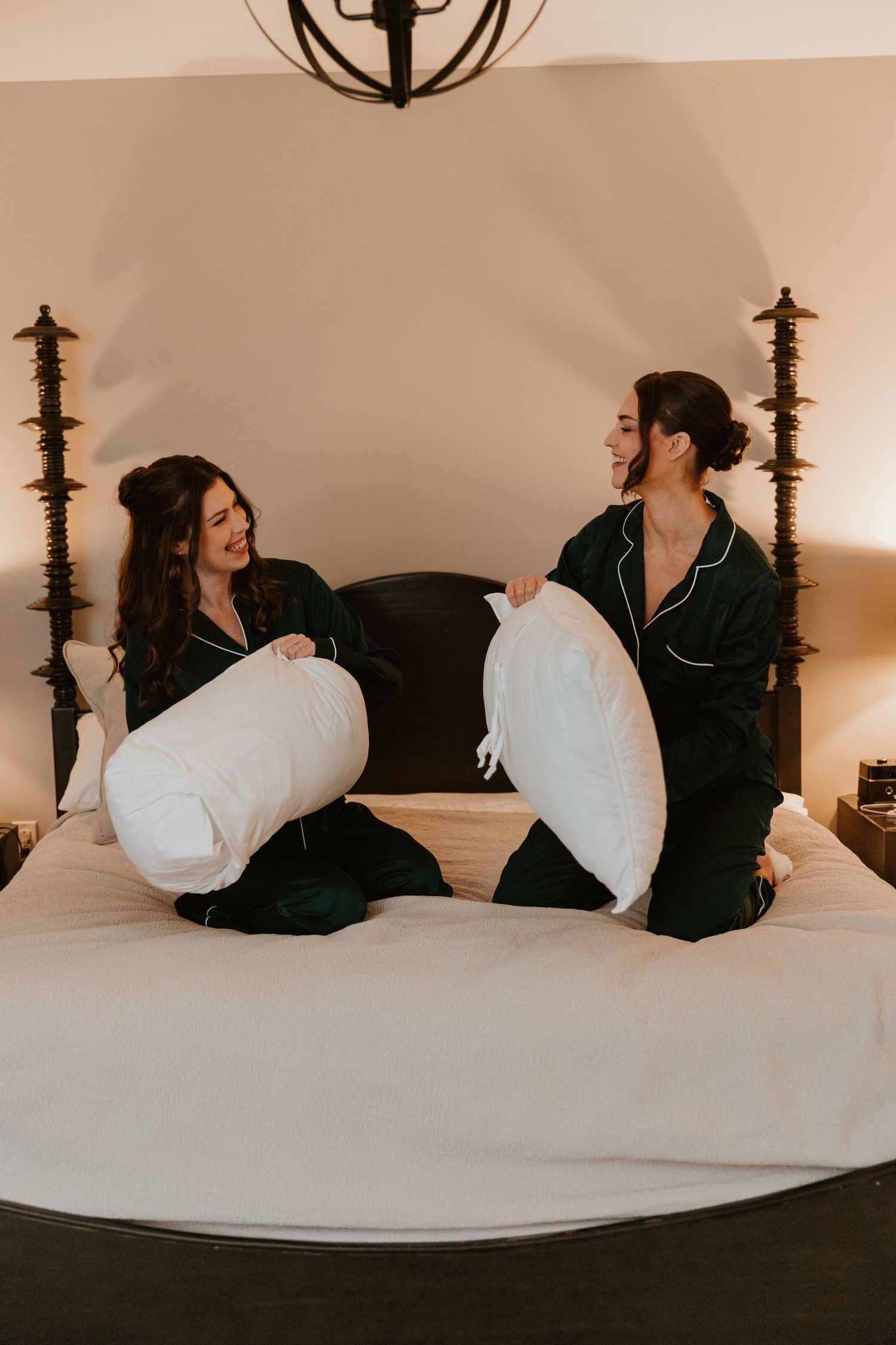 Two people in matching black pajamas having a pillow fight on a bed.