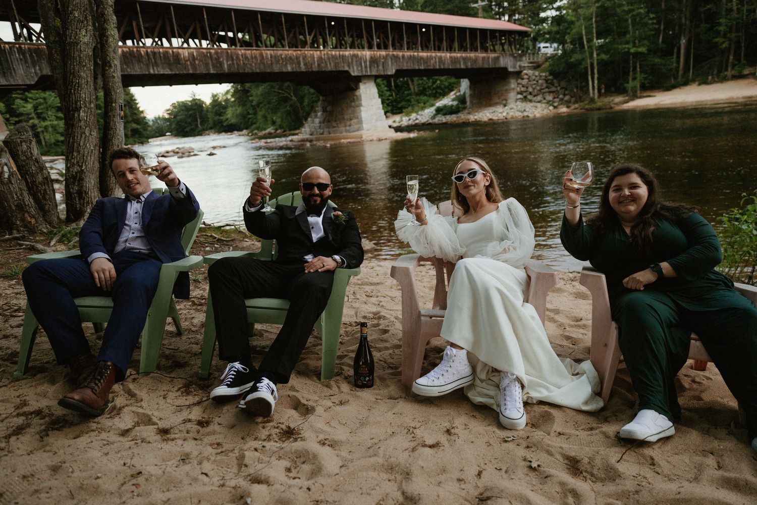 Wedding party relaxing in green Adirondack chairs along a riverbank.