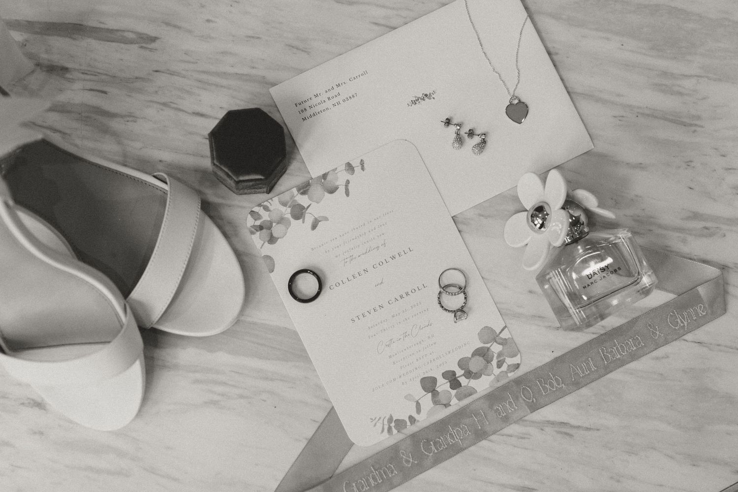 Black and white photo of wedding details including rings, shoes and invitation.