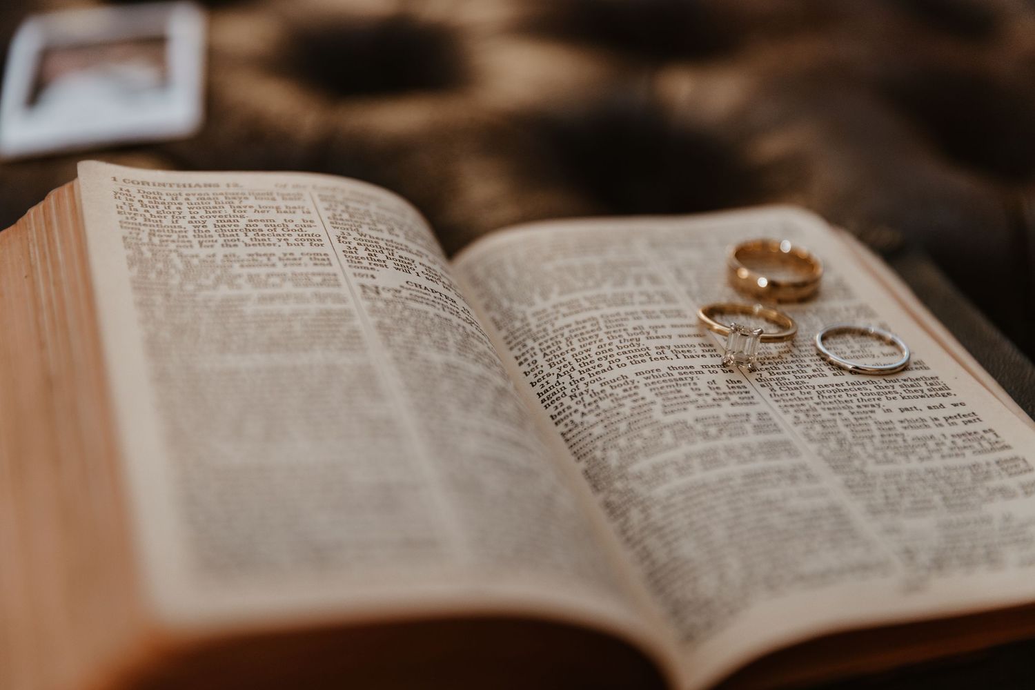 Wedding rings rest on open pages of a Bible in warm lighting.