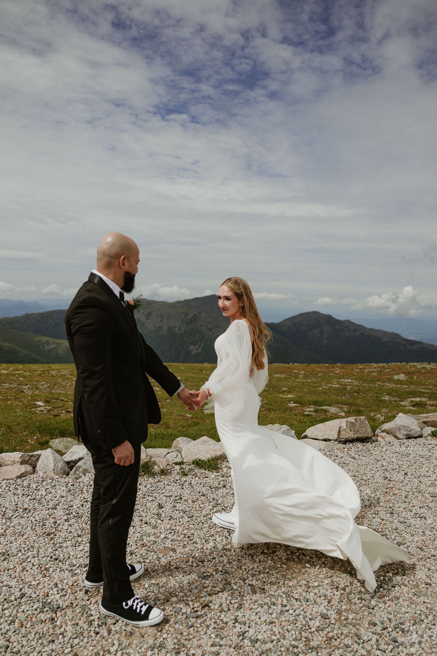 A dramatic mountain-top wedding photo with flowing white dress catching the wind.