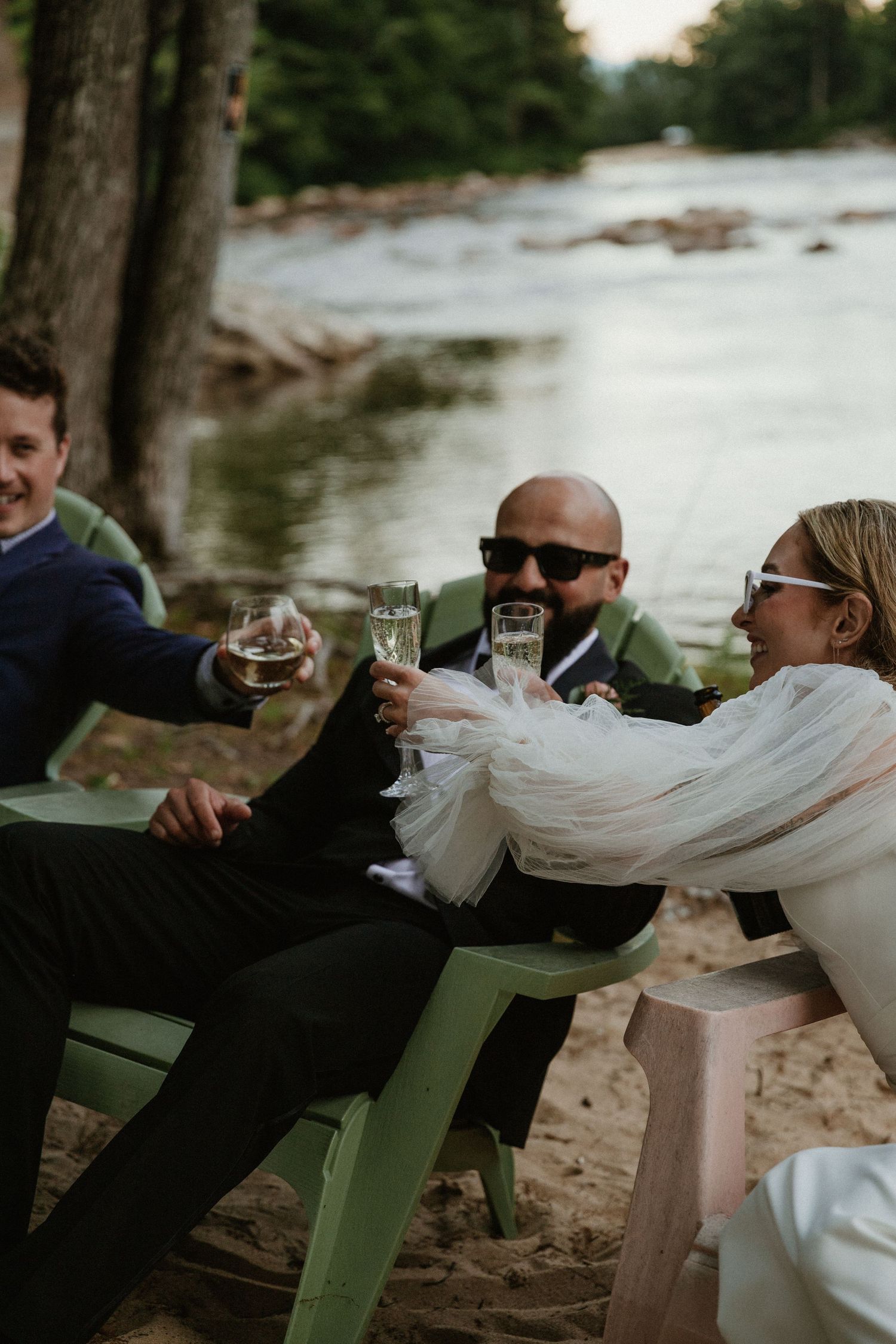 Wedding celebration with guests lounging in green chairs by a peaceful river.