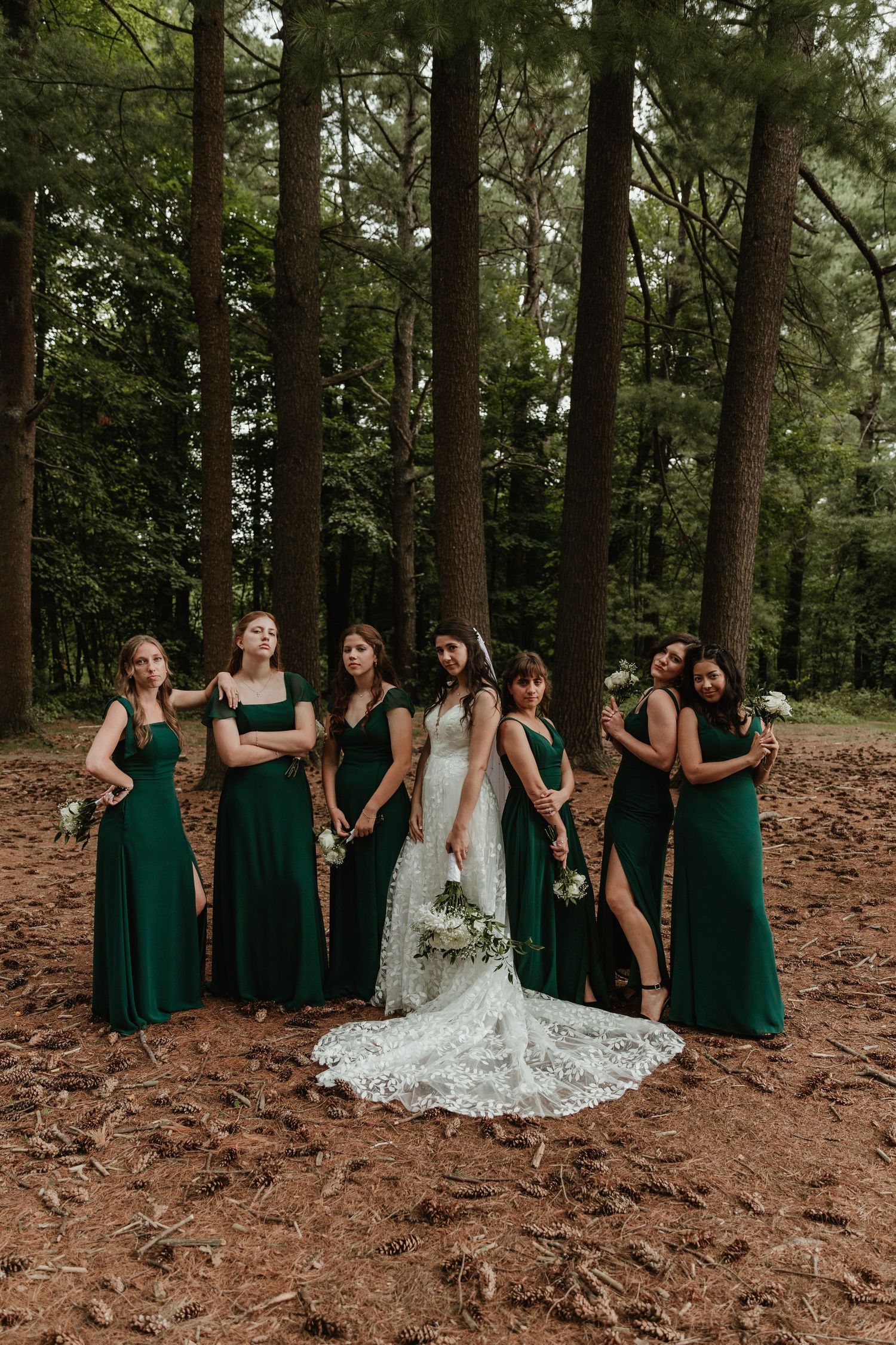 A bridal party in emerald green dresses poses together in a wooded forest setting.