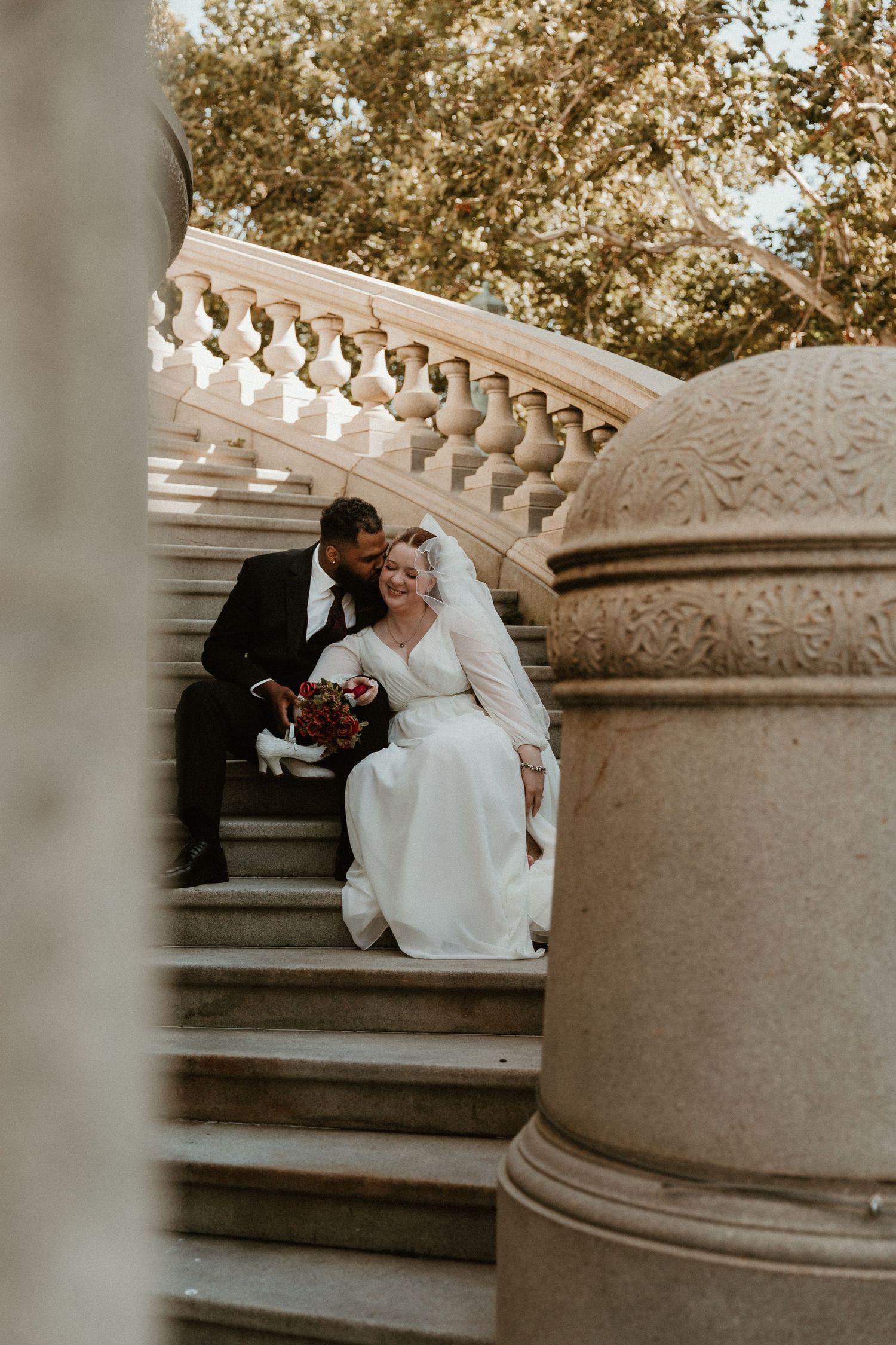 A couple shares a tender moment on ornate stone stairs during their wedding.