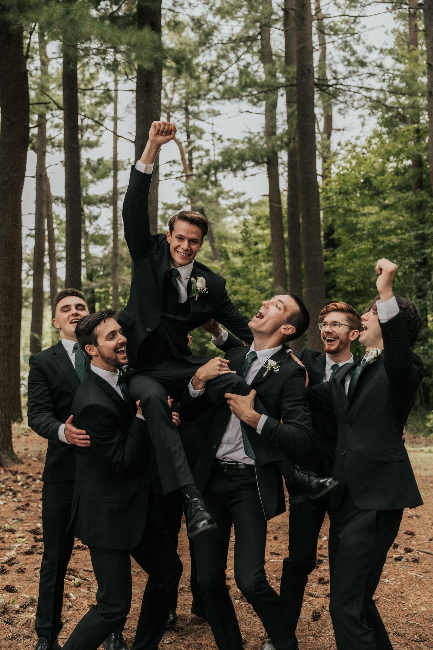 Wedding party of groomsmen jumping and celebrating in forest setting.