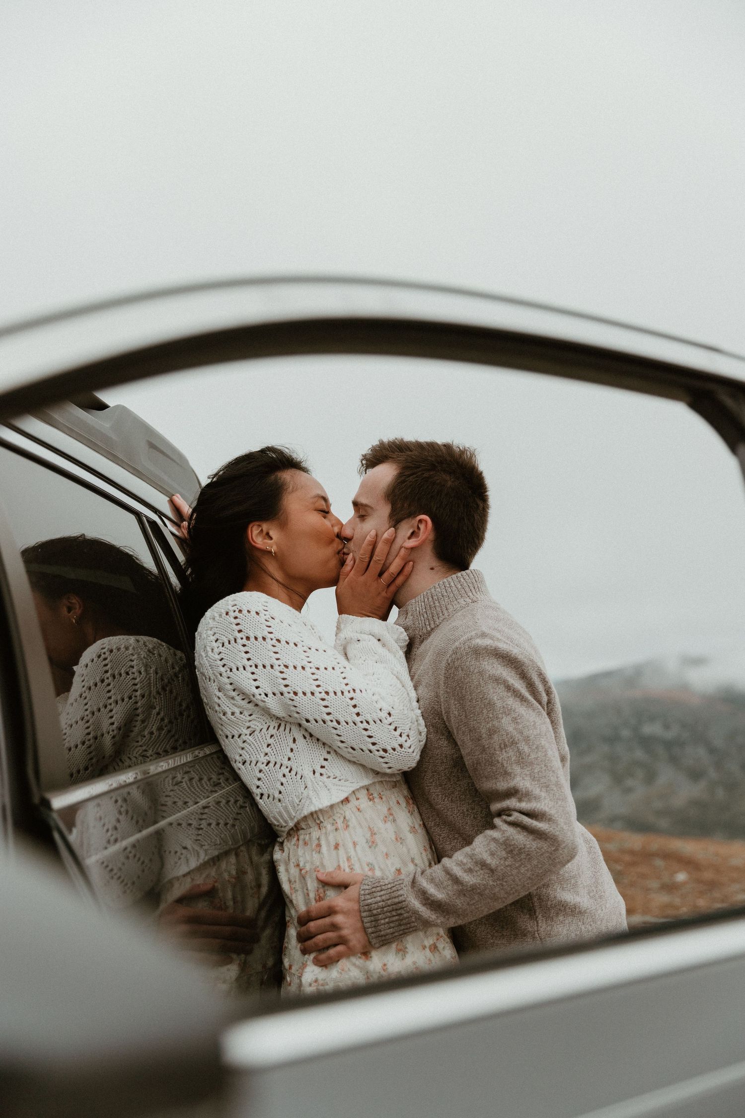 A romantic moment captured through a car window with mountains in the background.