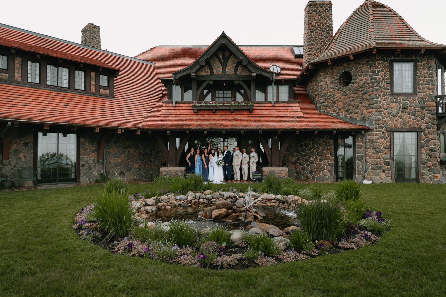 Stone and brick lodge with landscaped garden features and sloping green lawn in foreground.