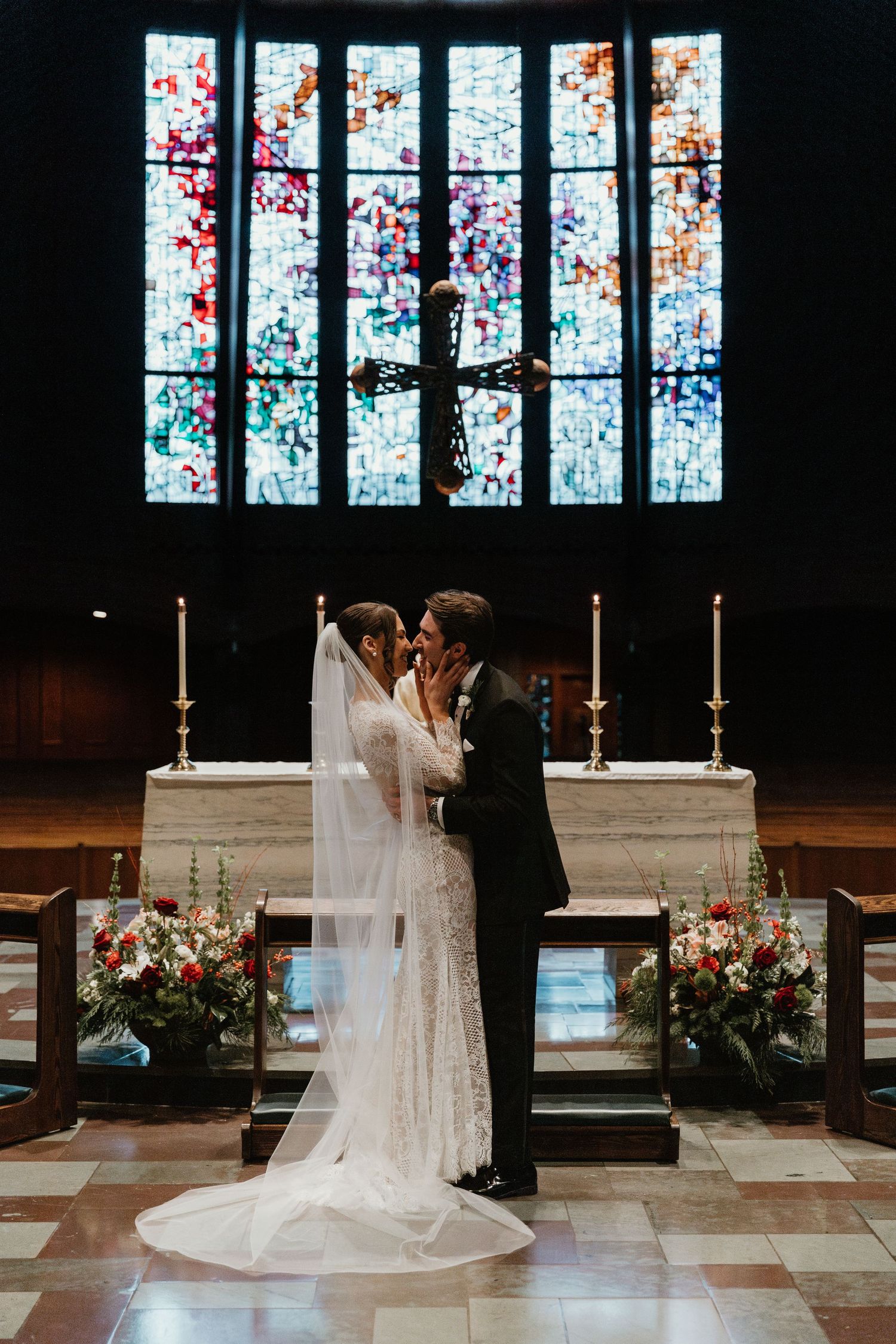 Couple sharing an intimate moment at the altar with colorful stained glass windows in the background.