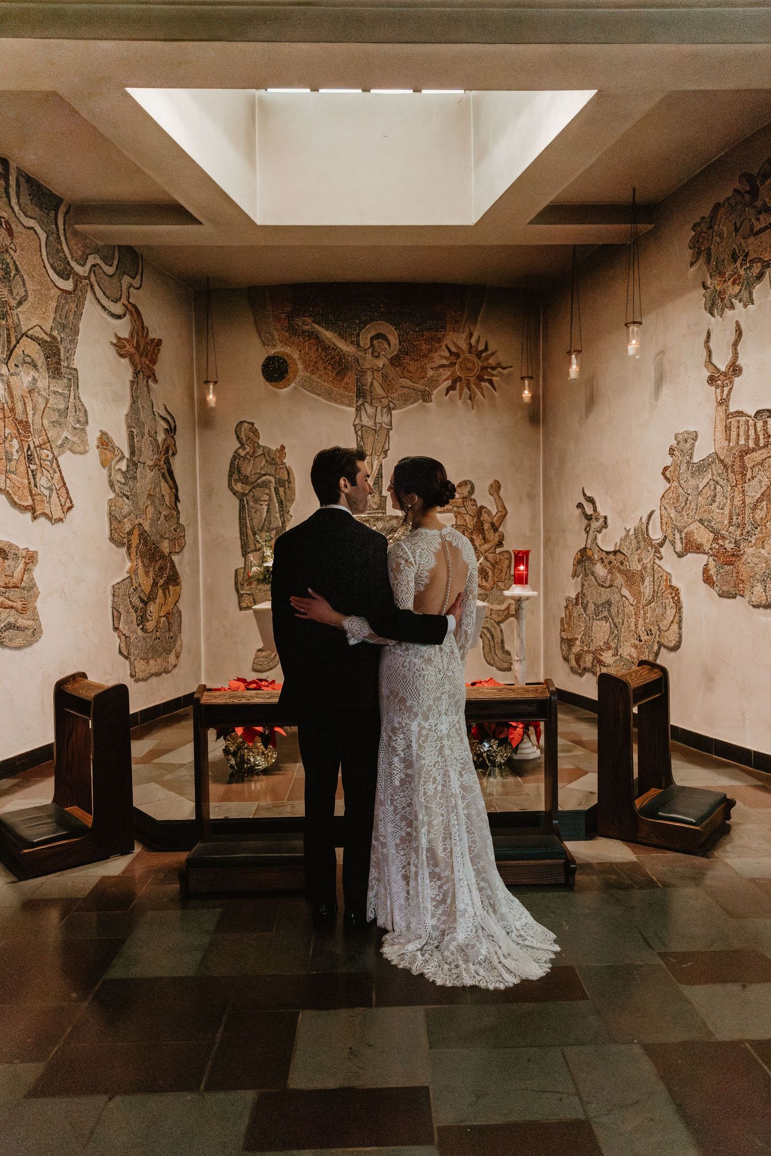 A couple stands together in formal attire viewing decorative wall murals in an intimate venue.