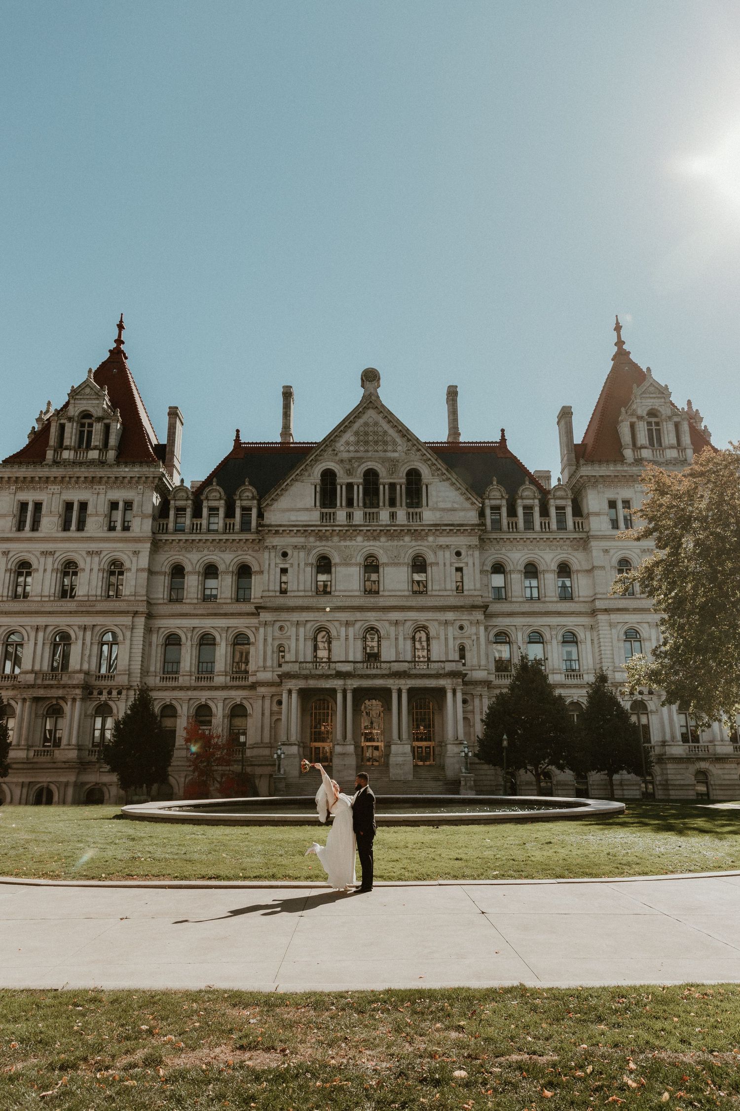 A couple poses in front of a grand historic mansion with Victorian architecture.