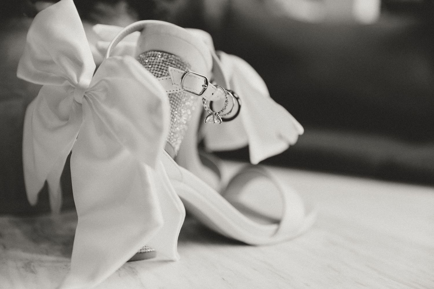 White satin ballet flats with bows and wedding rings displayed in black and white photography.