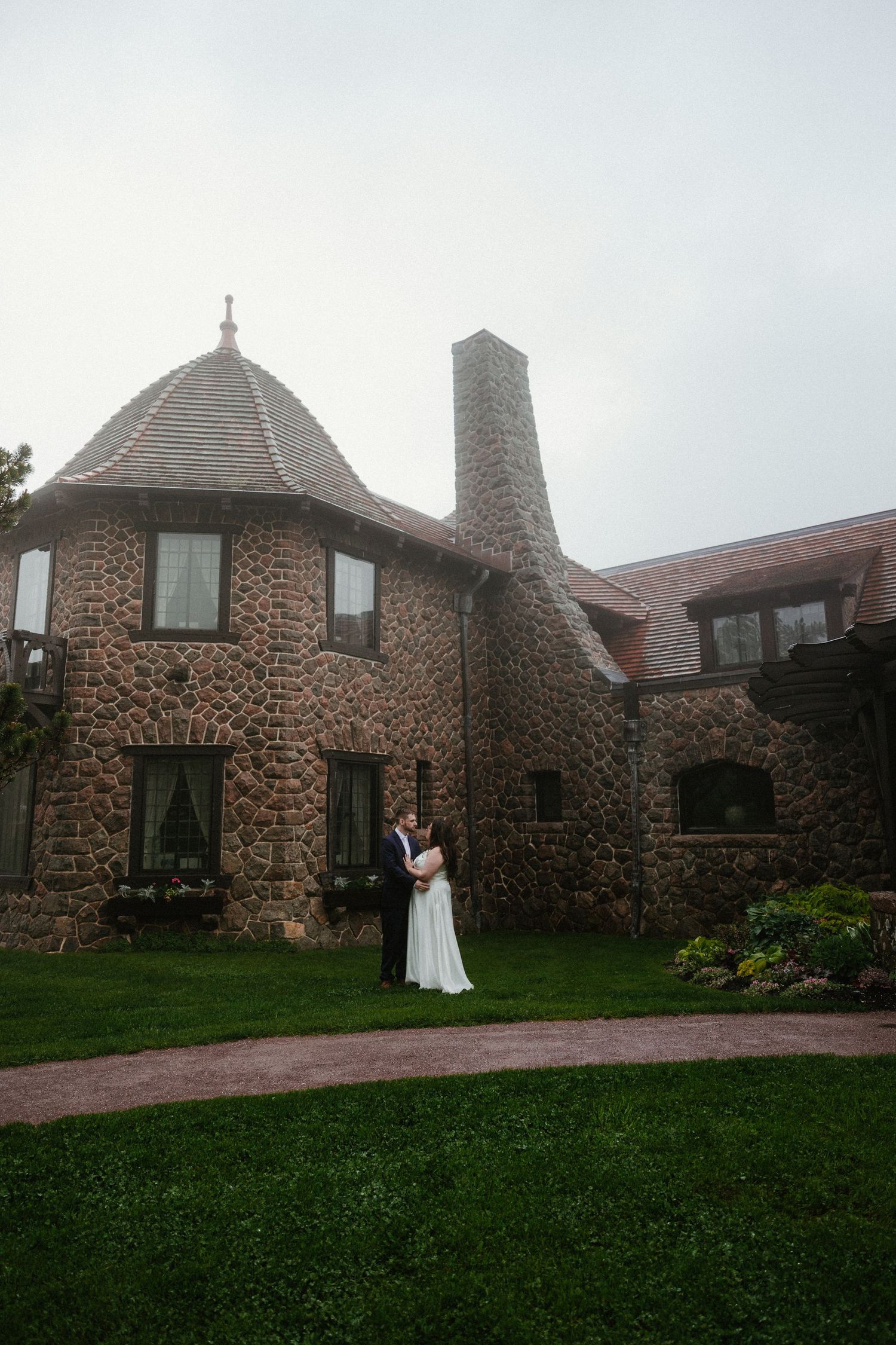 Stone castle-like building with turrets and brick chimneys on landscaped grounds.