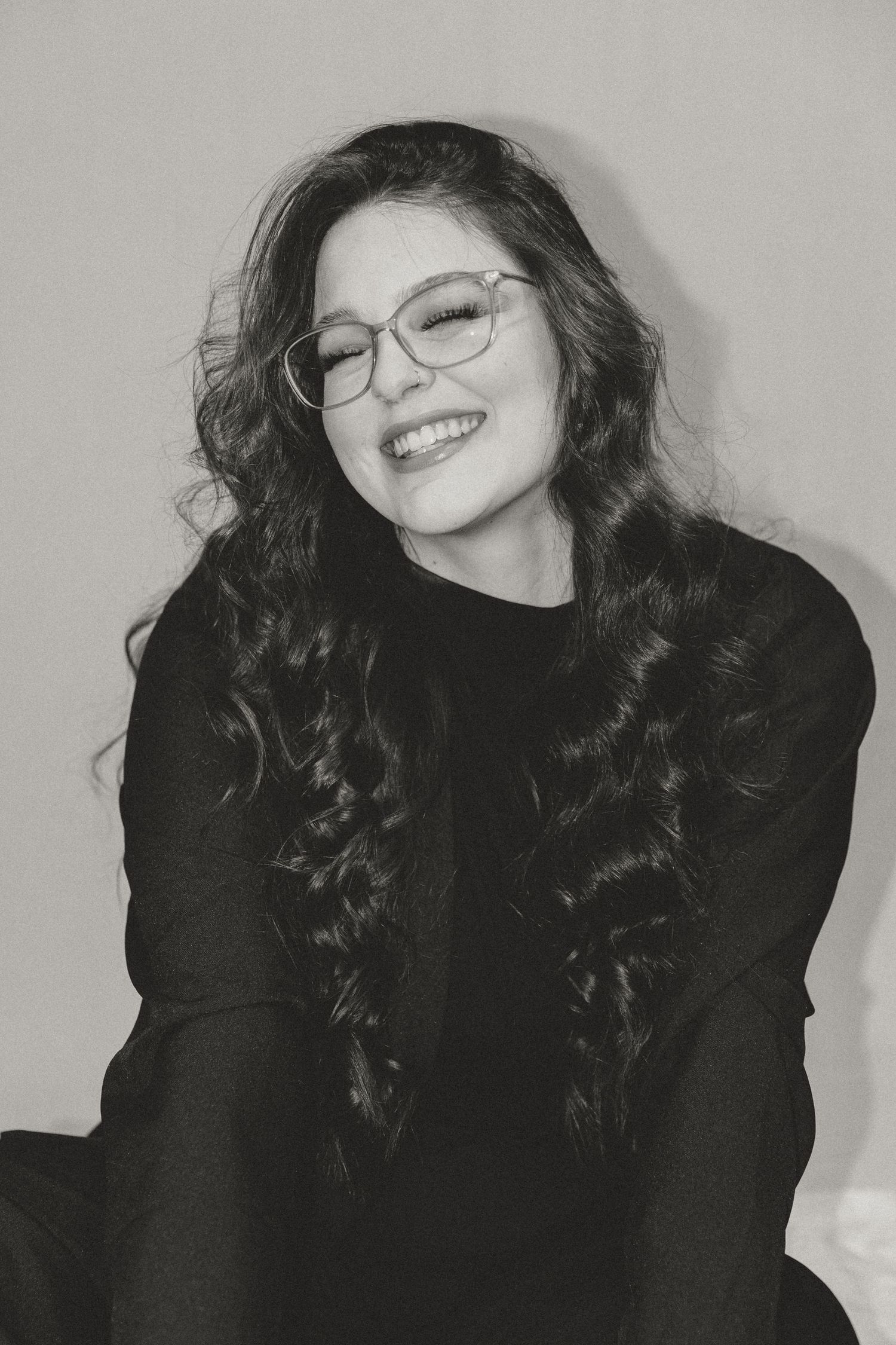 Black and white photo series showing person with dark curly hair and glasses laughing while wearing a black top.