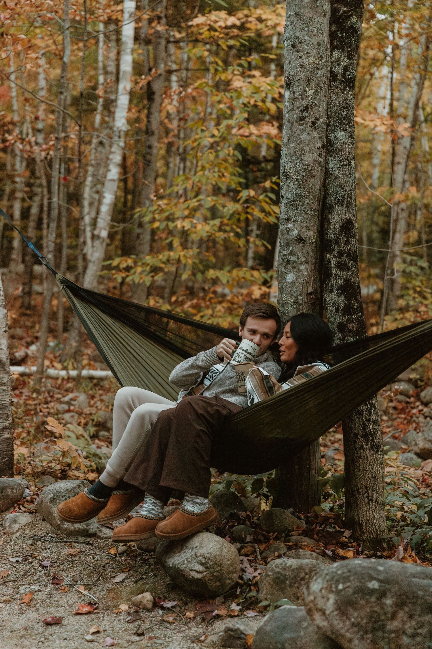 A couple relaxing together in a hammock surrounded by autumn forest trees.