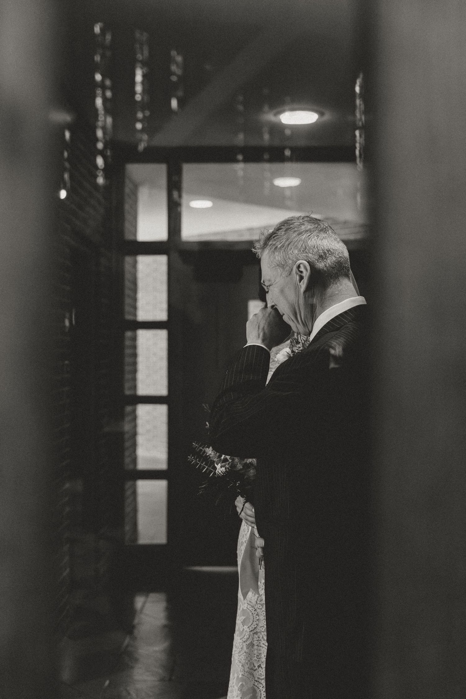 A black and white candid moment captured through a doorway during a wedding.