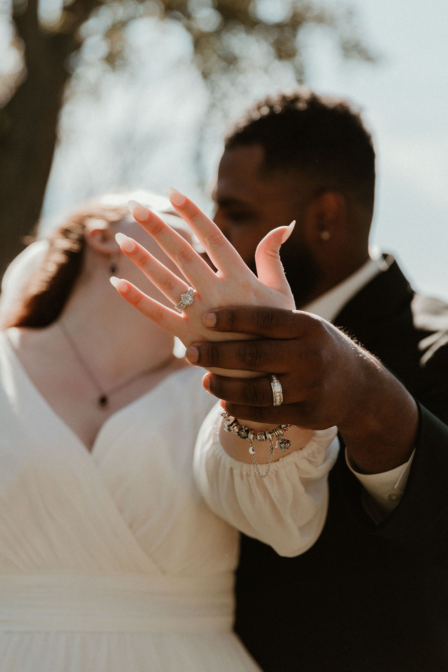 Close-up of newlyweds' hands showing wedding rings in natural sunlight.