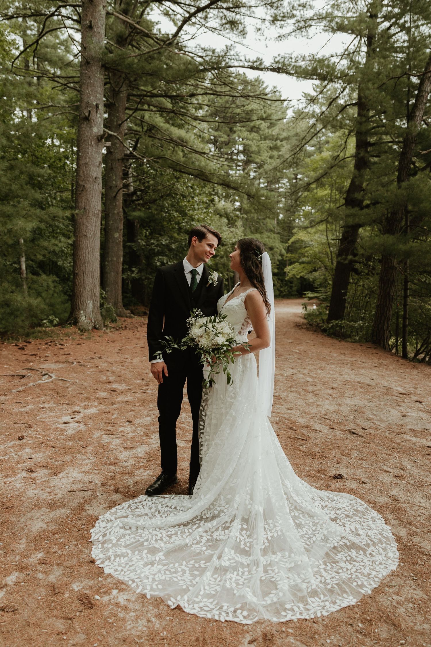 A stunning lace wedding dress with a long train photographed in a wooded forest setting.