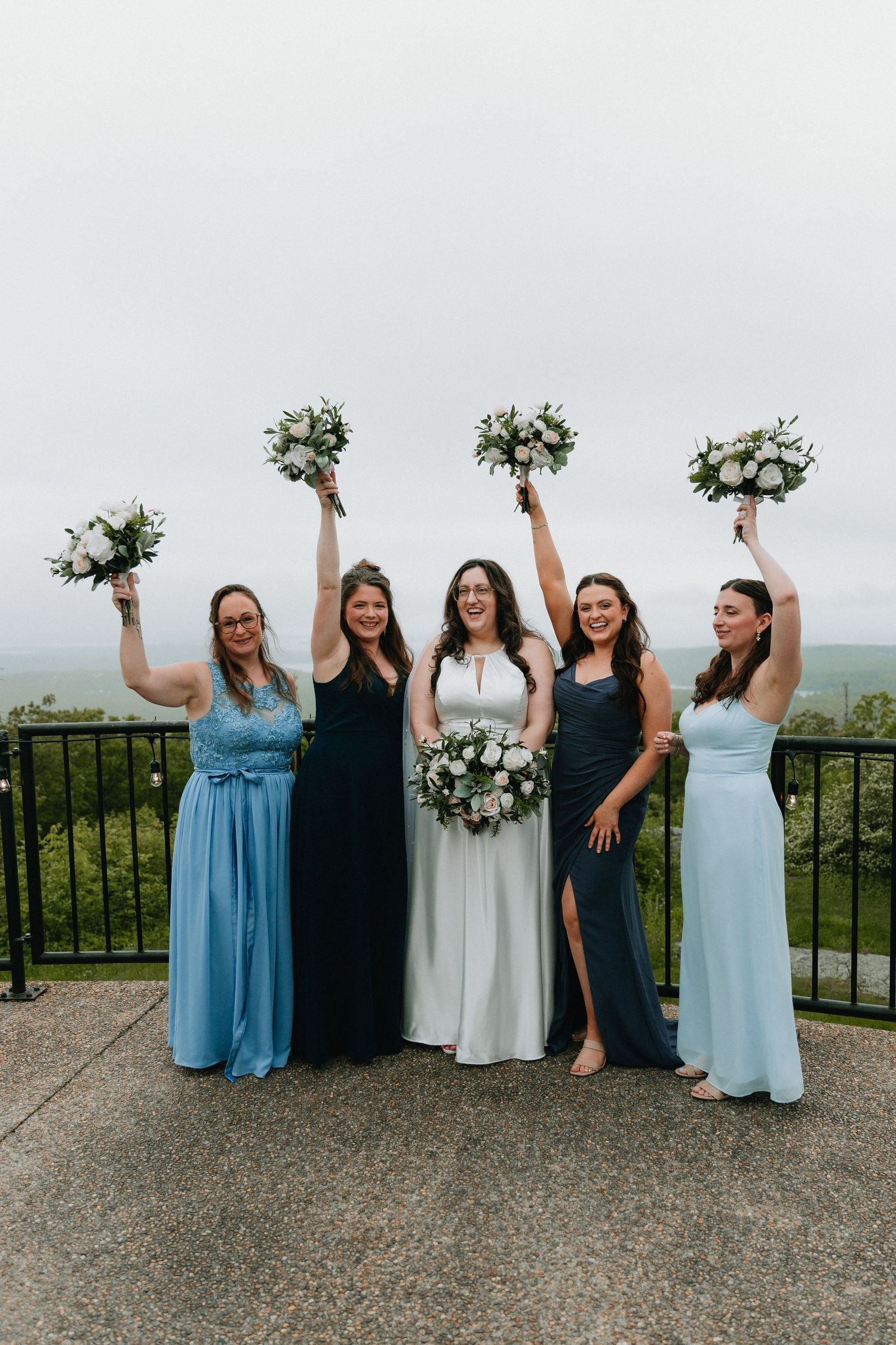 Bridesmaids celebrating with raised bouquets against mountain backdrop.