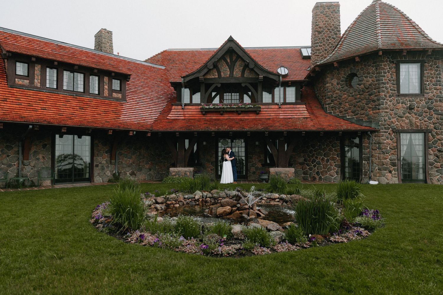 Panoramic view of historic stone mansion with red roof tiles and landscaped grounds.