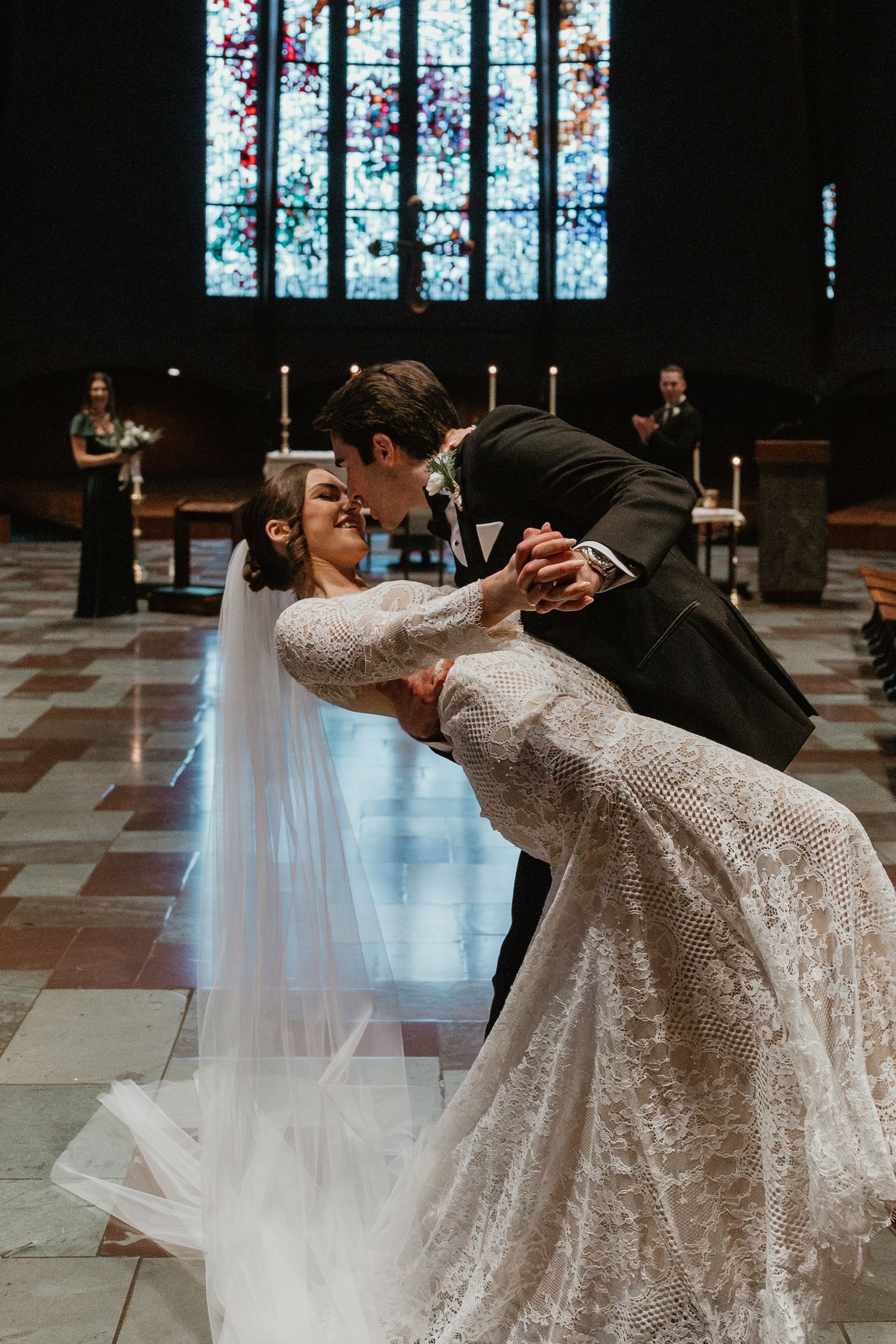 A romantic dip dance move between newlyweds in a church with stained glass windows in the background.