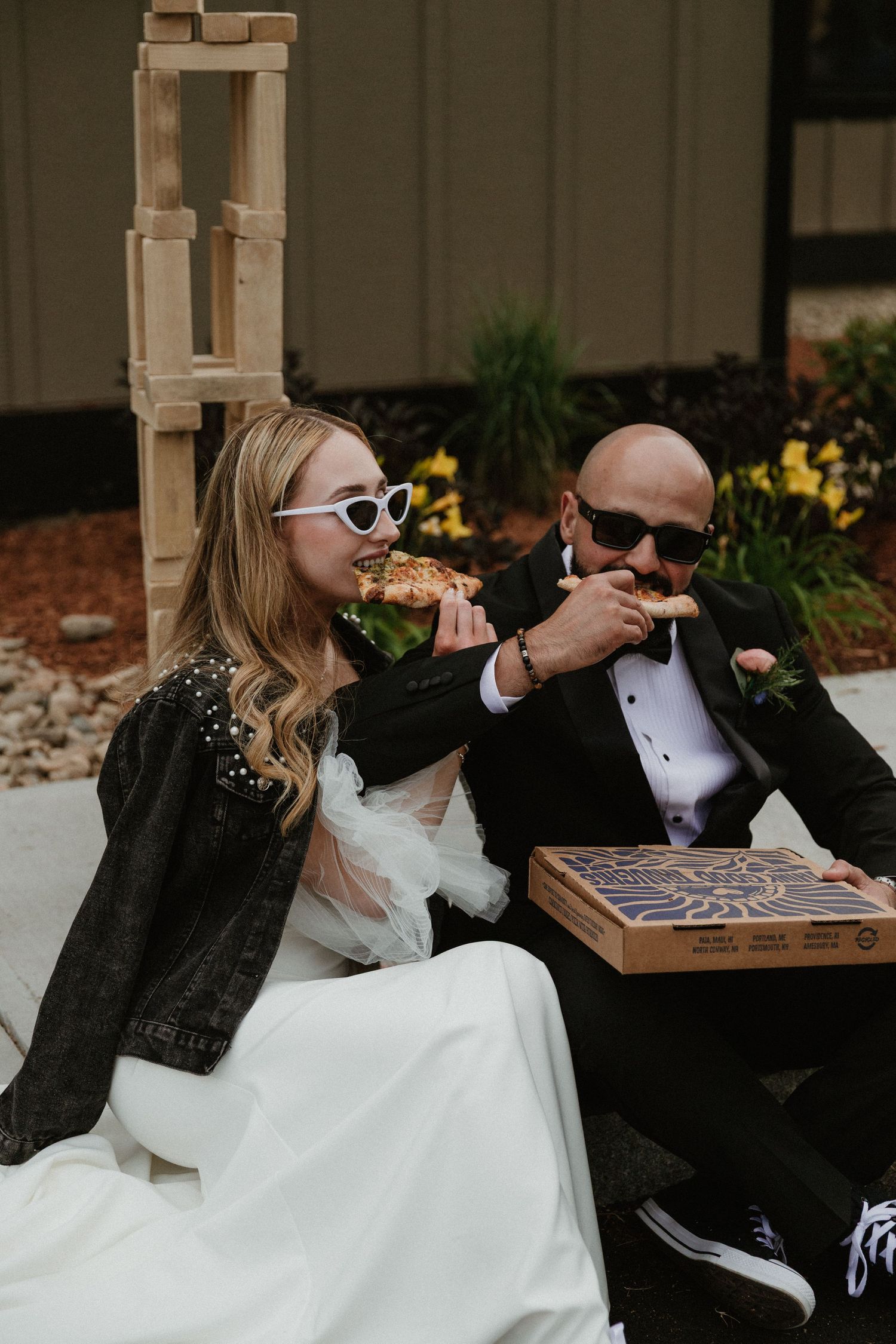 Wedding couple sharing drinks and laughter while sitting at an outdoor table.