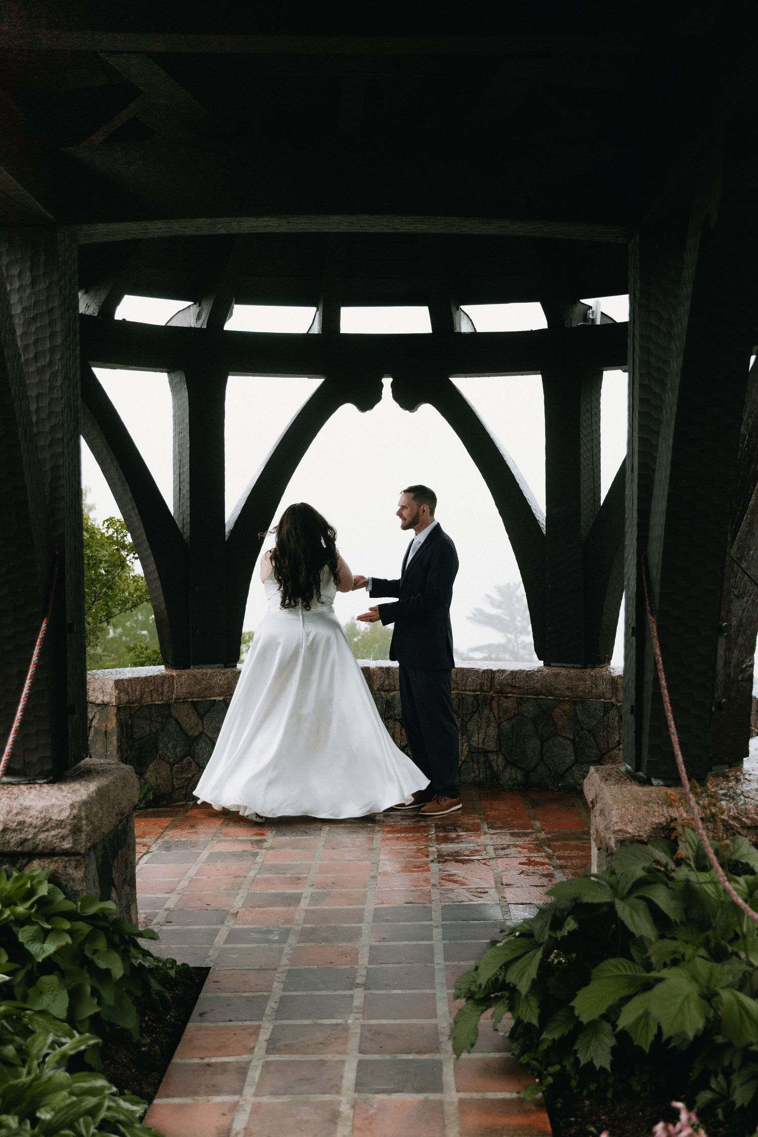 A covered stone terrace with dramatic wooden beams frames a misty mountain view.