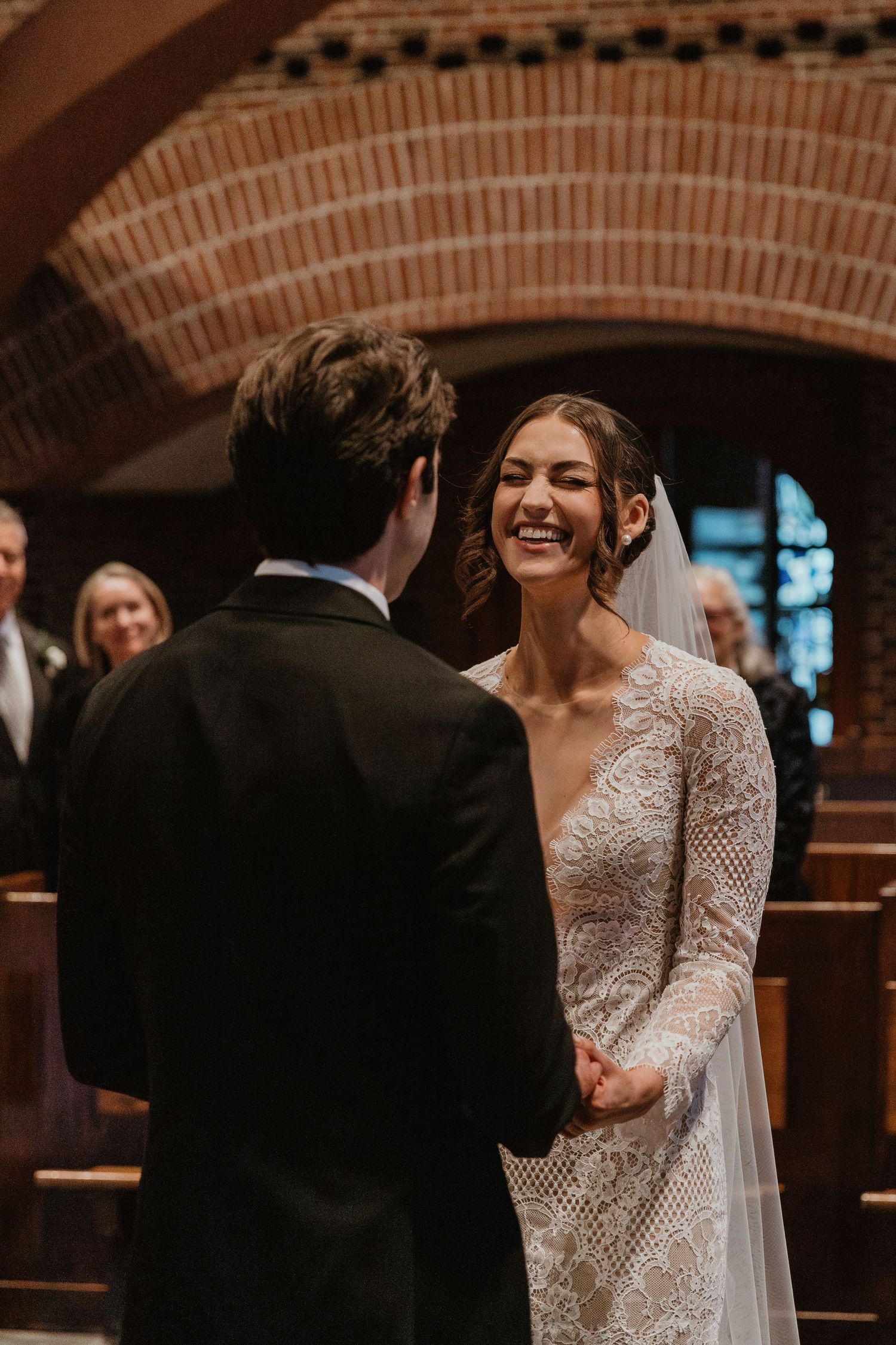 A bride and groom share a joyful moment during their wedding ceremony inside a brick-arched church.