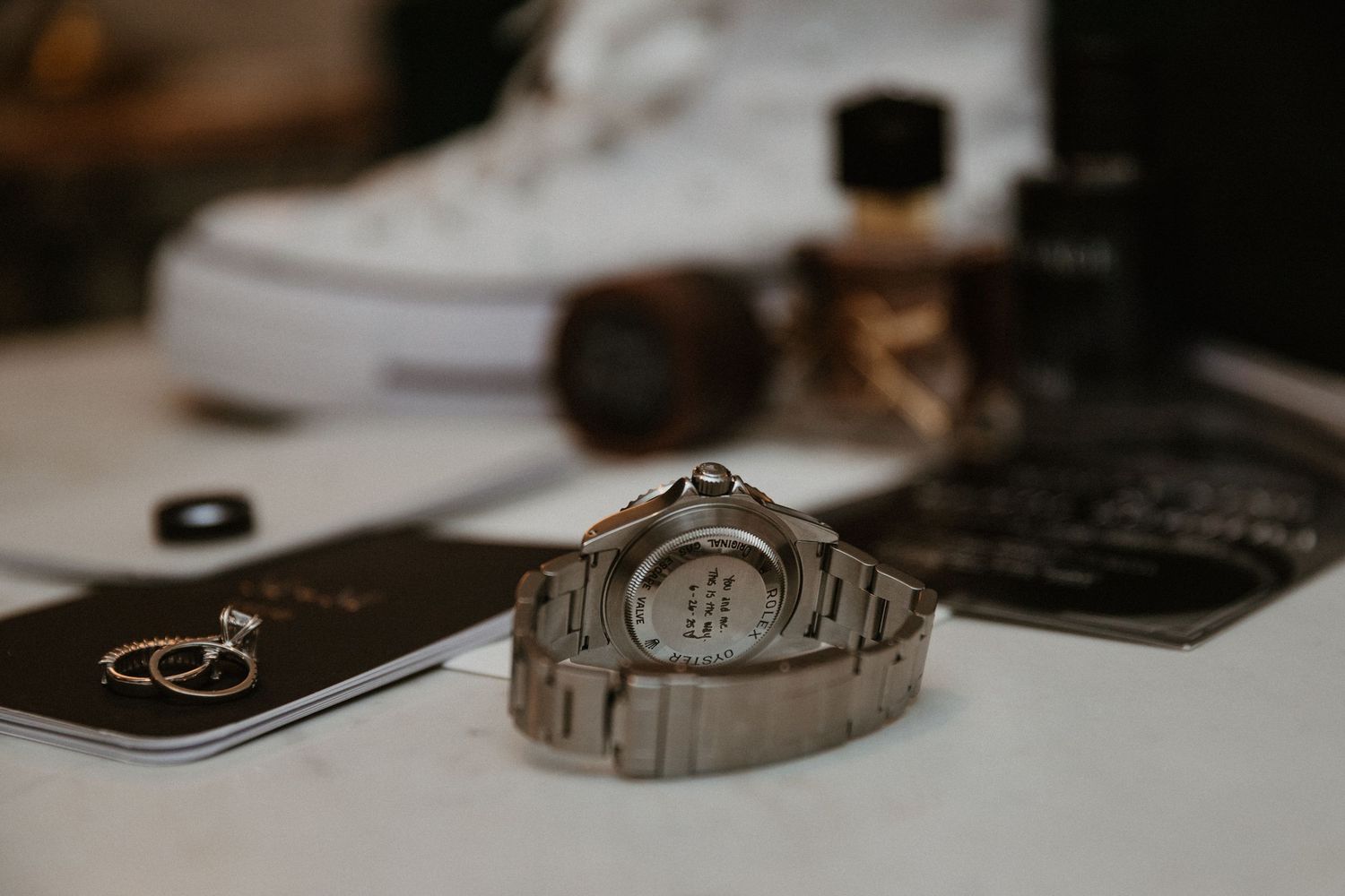A silver watch and wedding stationery arranged on a white surface with sneakers in the background.