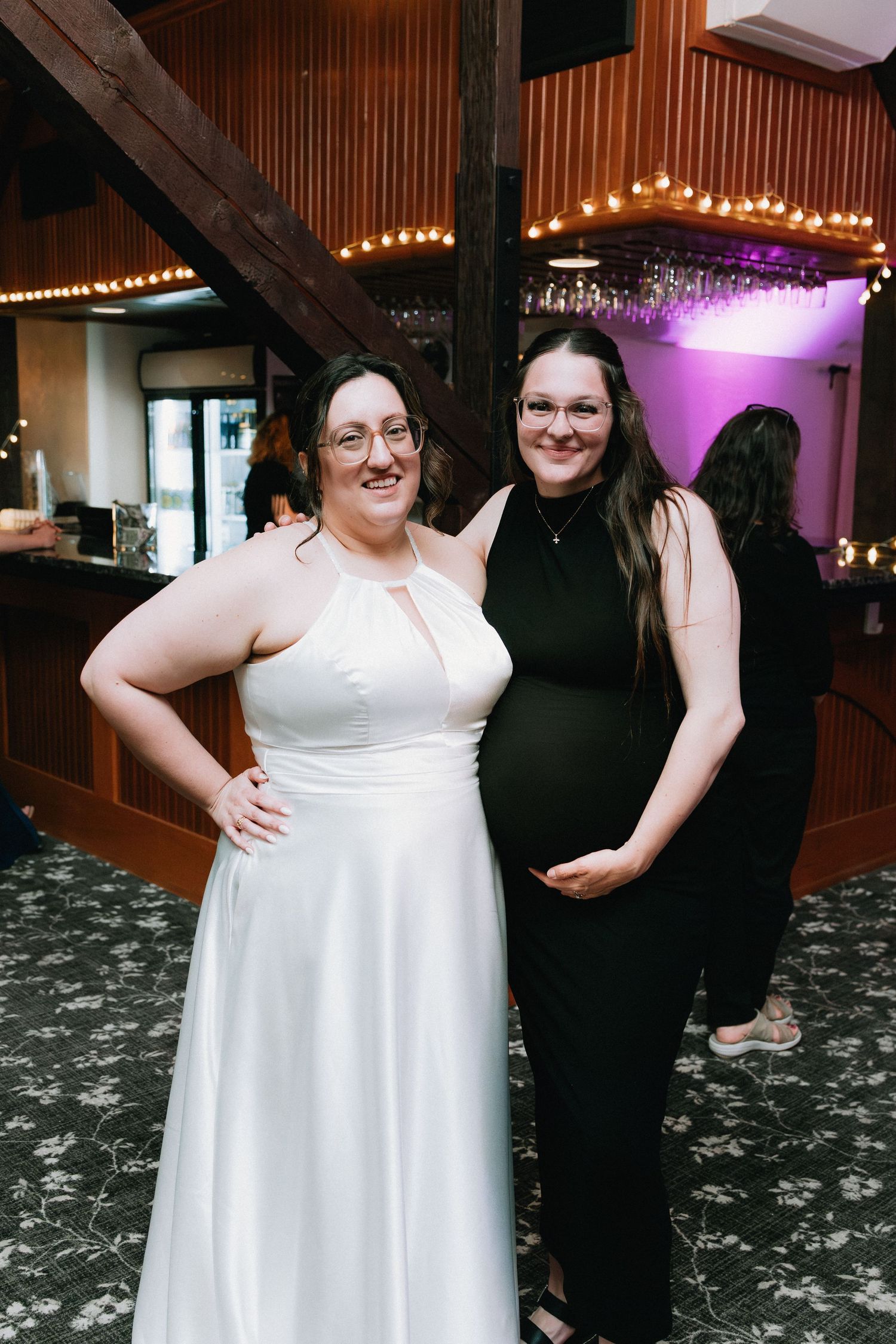 A couple in formal attire dancing and laughing together at a wedding reception with string lights in the background.