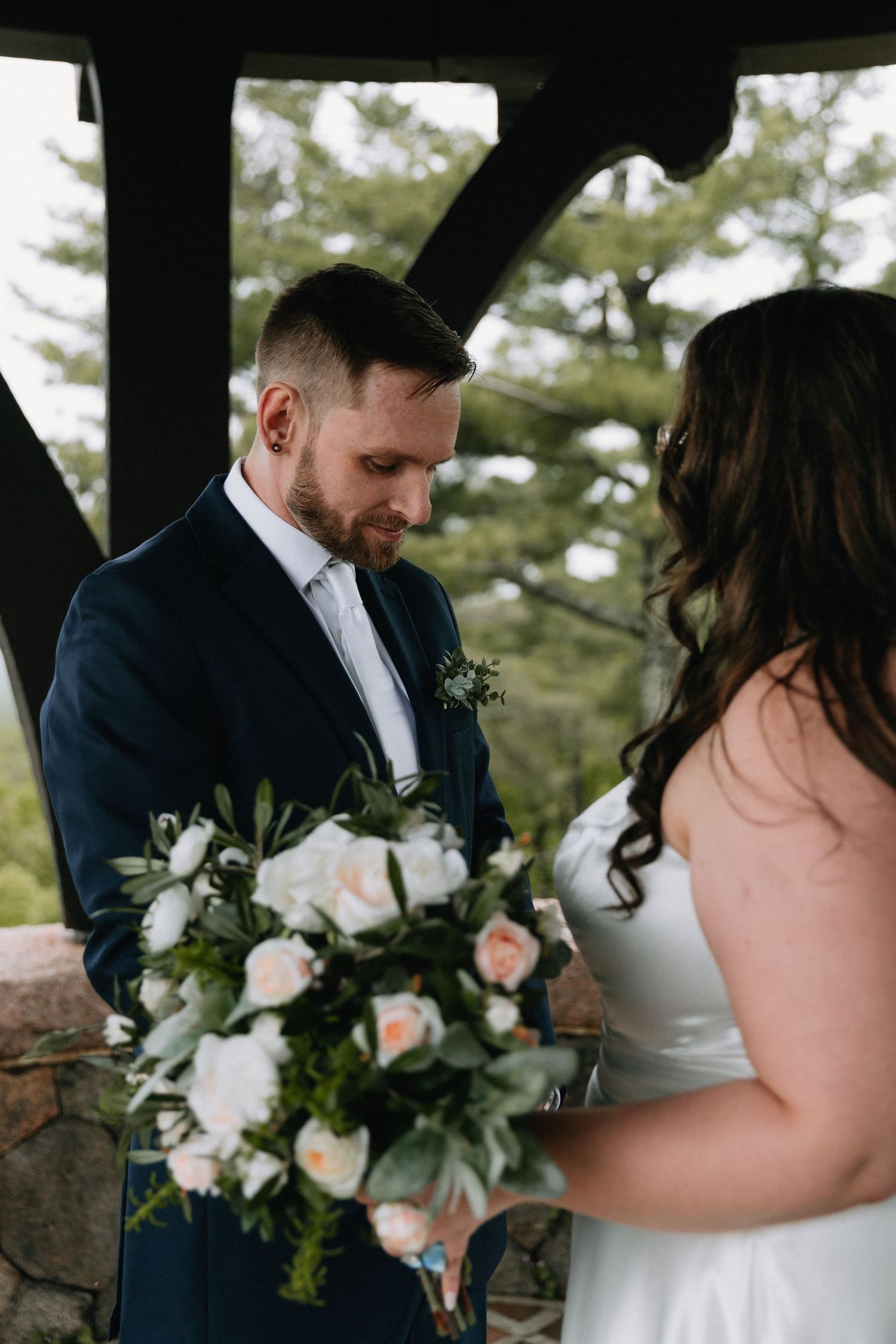 Intimate wedding moment captured under a wooden pavilion with elegant floral arrangements.