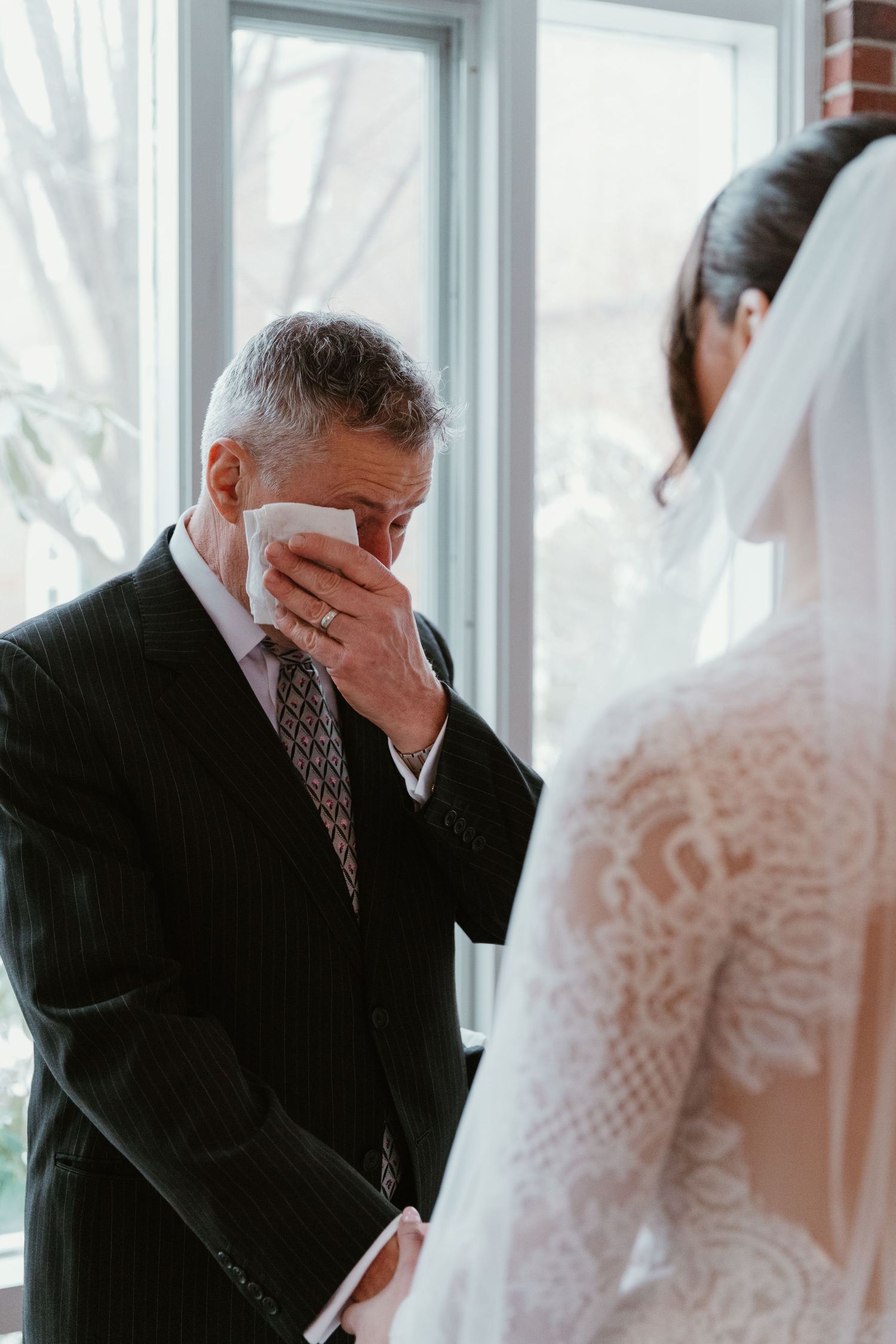 An emotional moment captured during a wedding ceremony near bright windows.