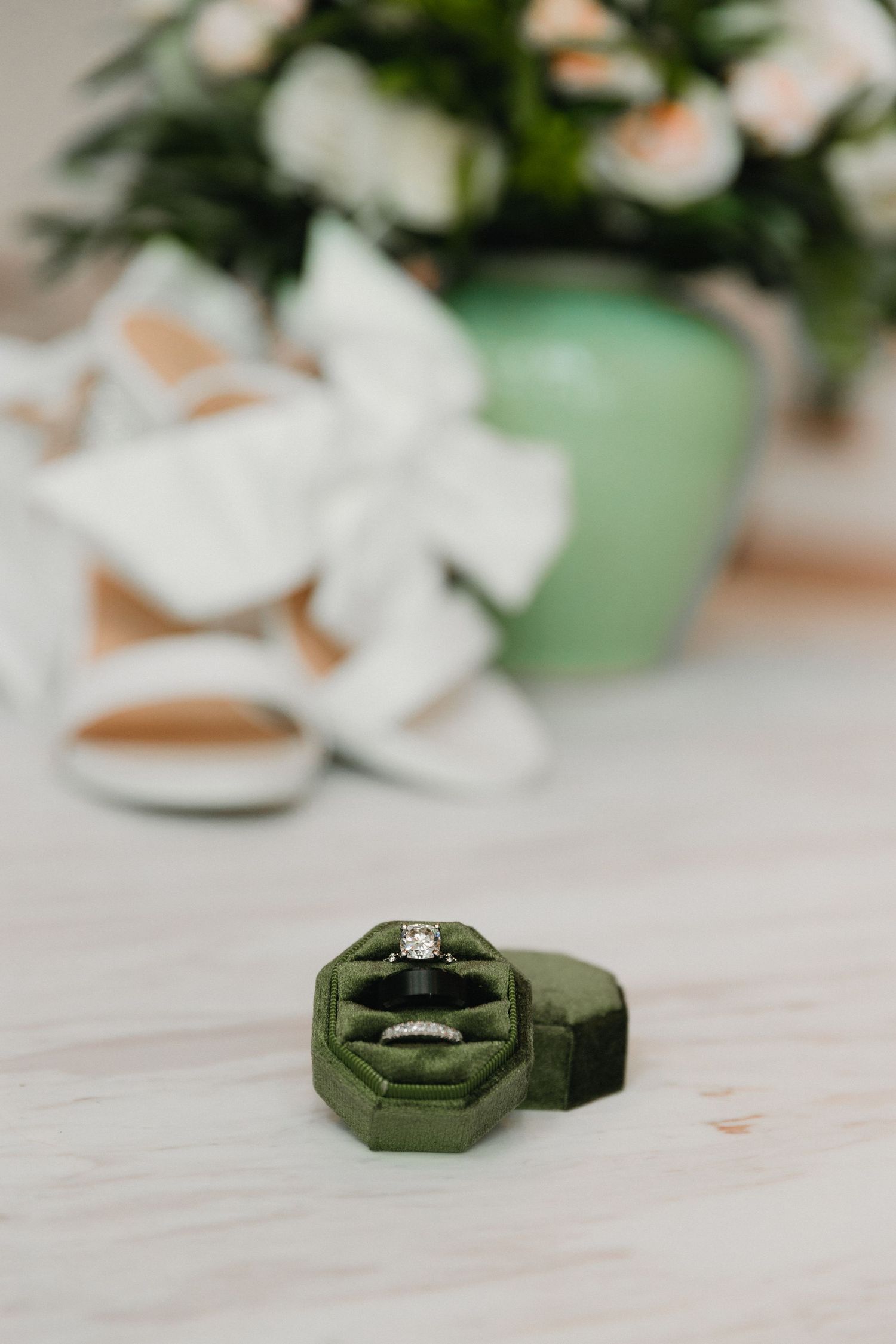 A diamond engagement ring in green velvet box with wedding shoes in background.
