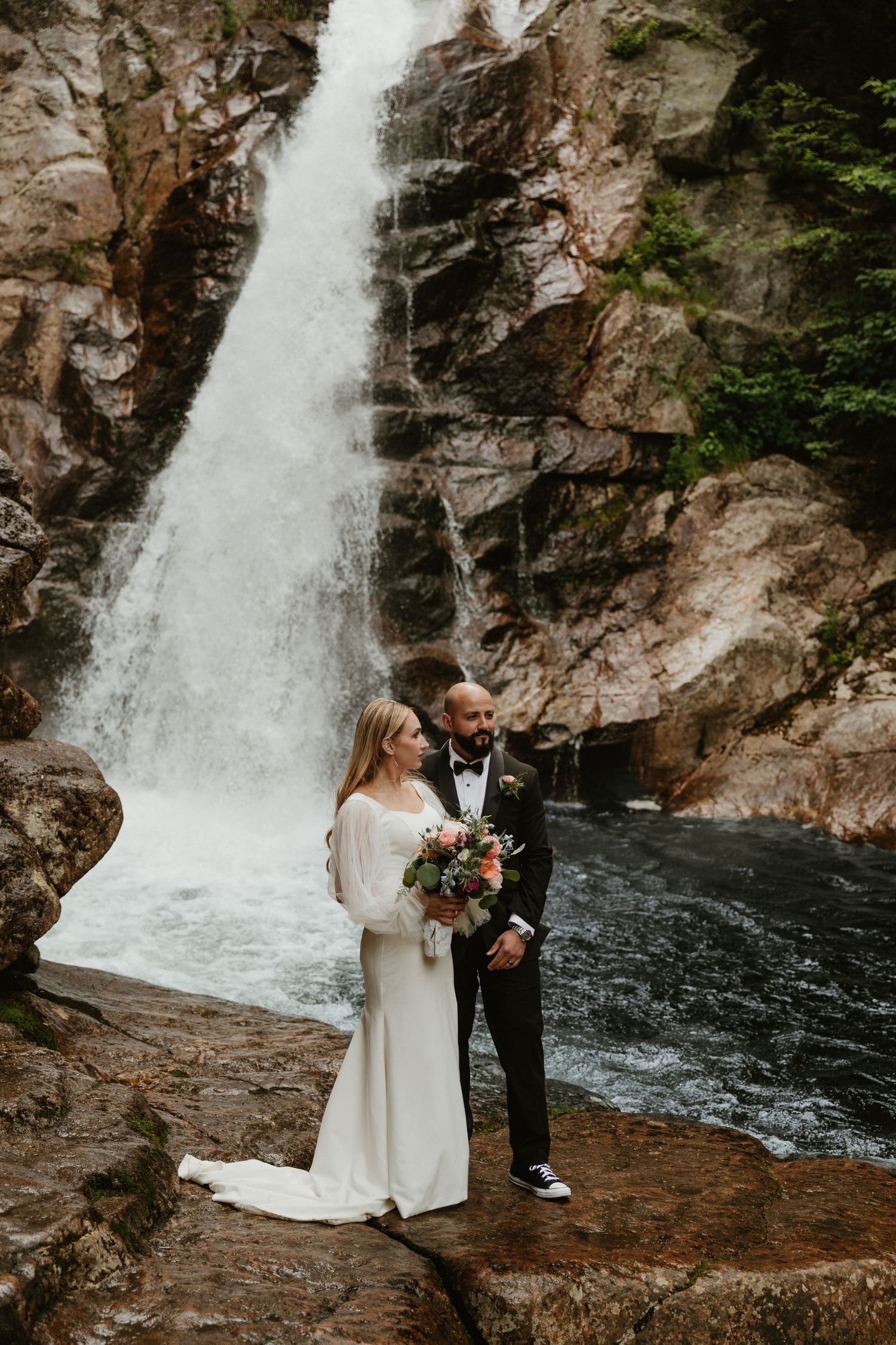 Intimate wedding ceremony photos captured in front of a dramatic cascading waterfall in a rocky forest setting.