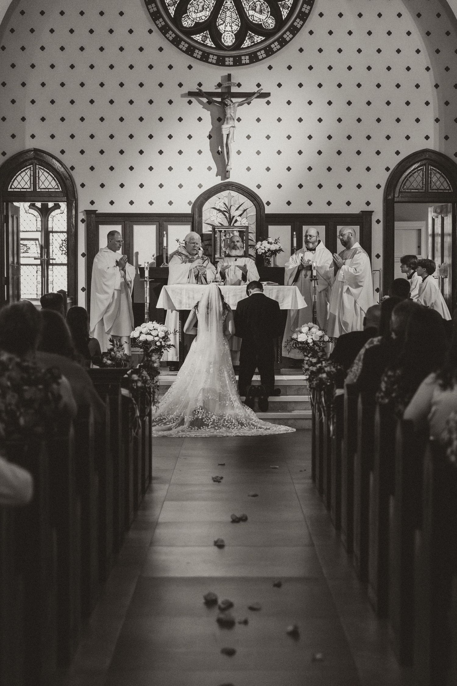 Black and white photo of a traditional church wedding ceremony with dotted wallpaper and arched windows.