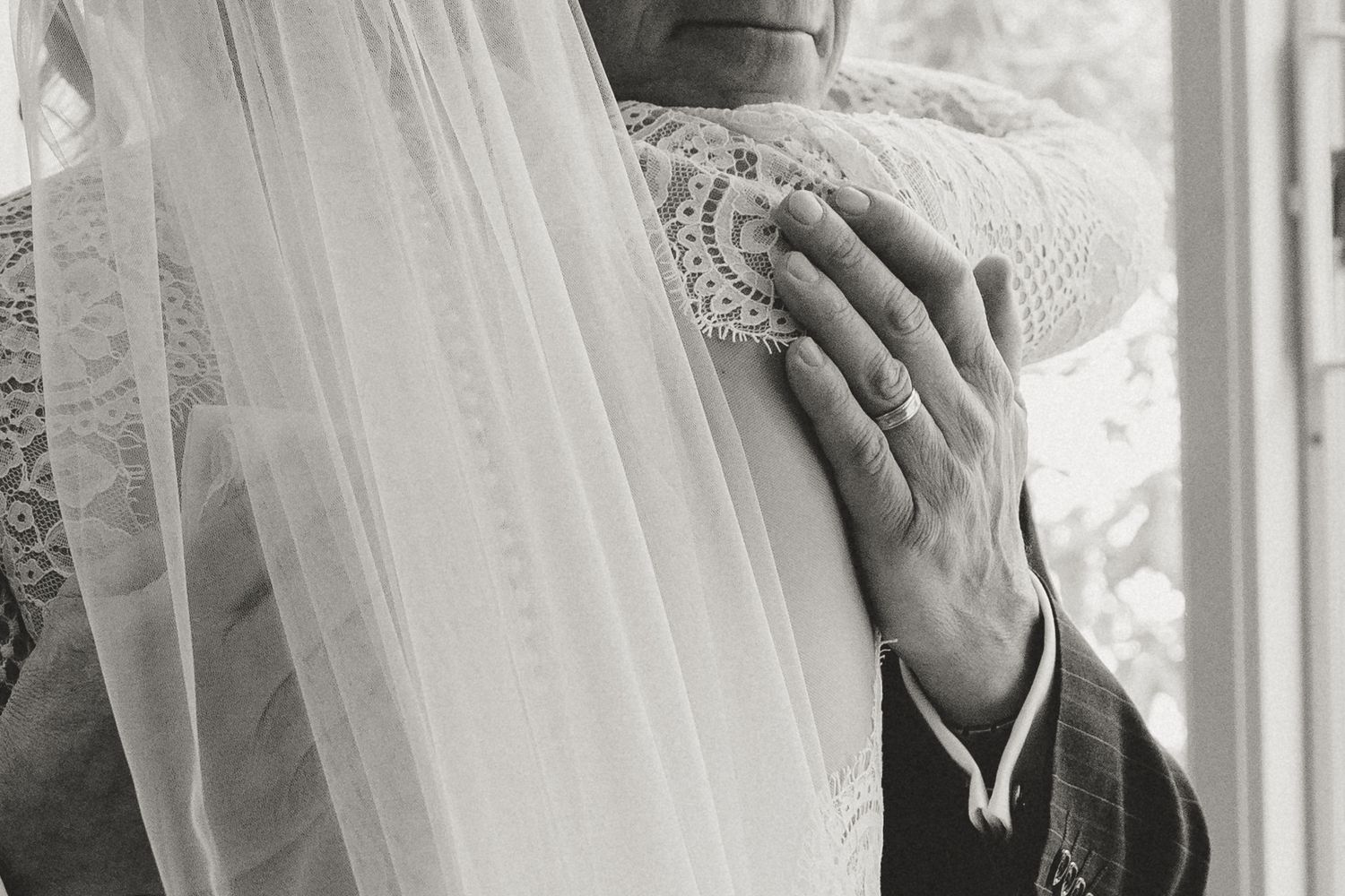 Close-up black and white photo of hands touching delicate wedding veil lace.