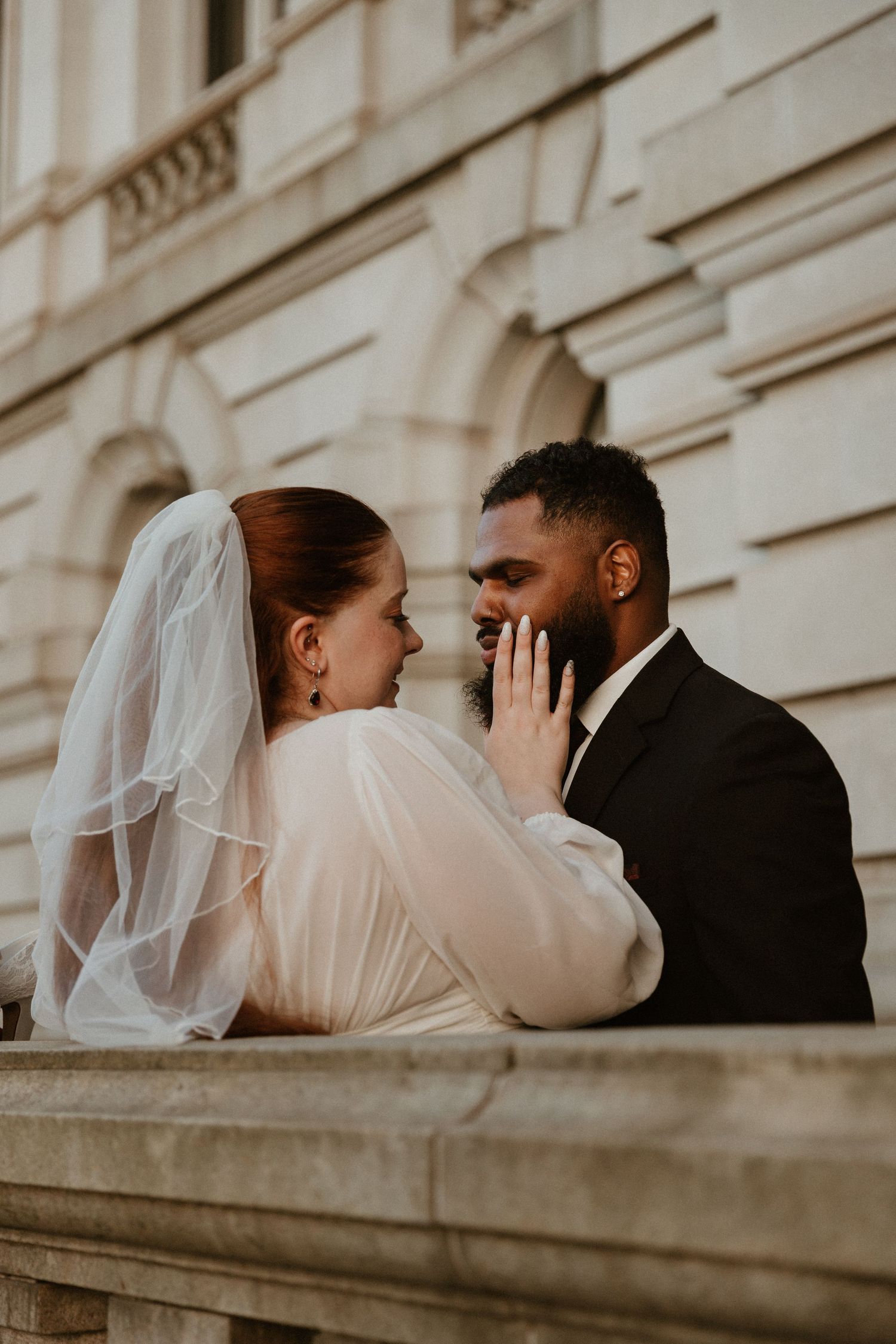 Romantic wedding couple shares intimate moment on historic building balcony.
