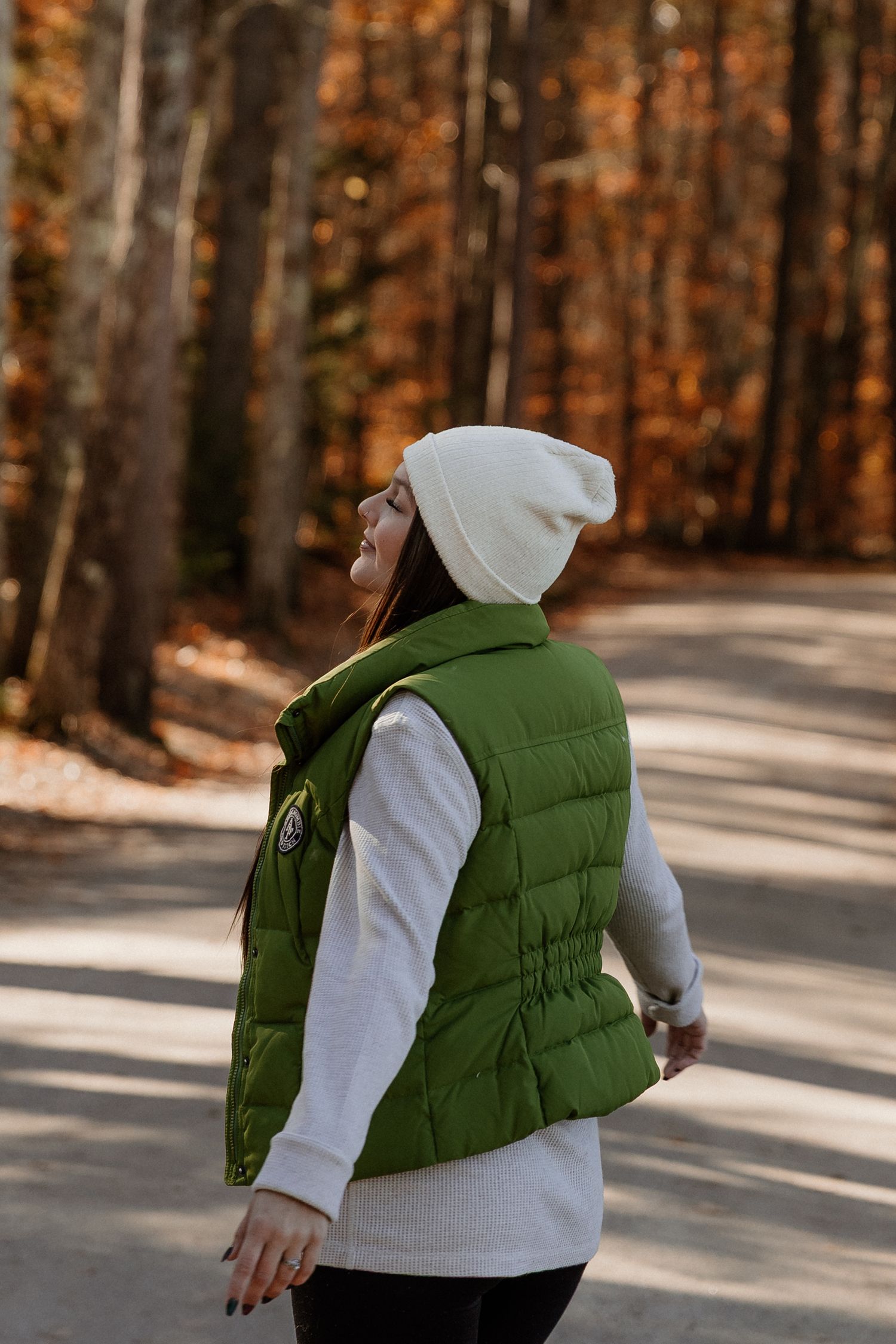 Four sequential shots of a person wearing a green puffer vest and white sweater against an autumn forest backdrop.