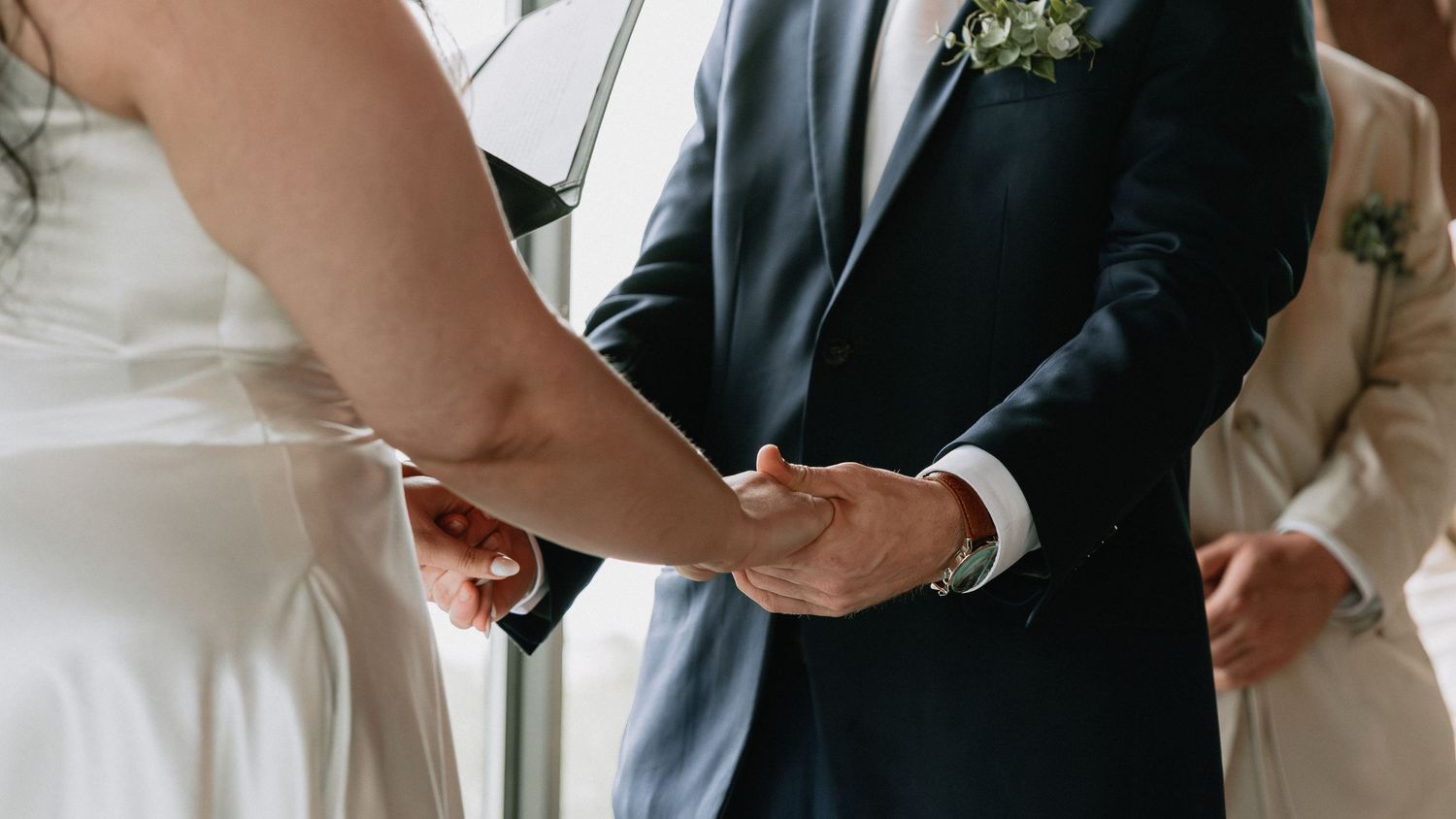 Close-up details of formal wedding attire showing suits and dresses in neutral tones.