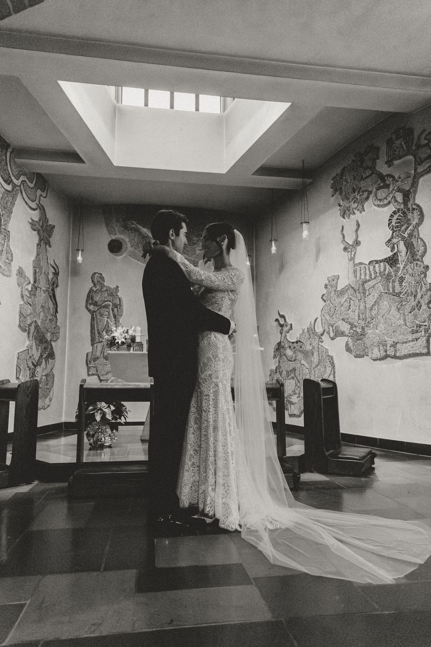 A black and white photo of a couple dancing in a room with artistic wall murals.