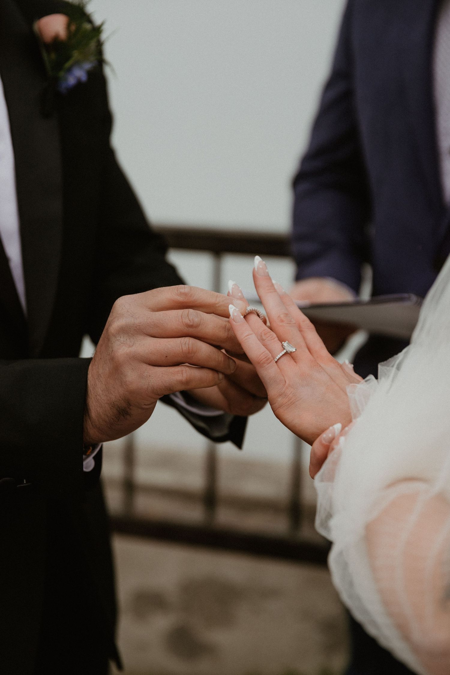 Detailed shot of wedding ring exchange between couple in formal attire.