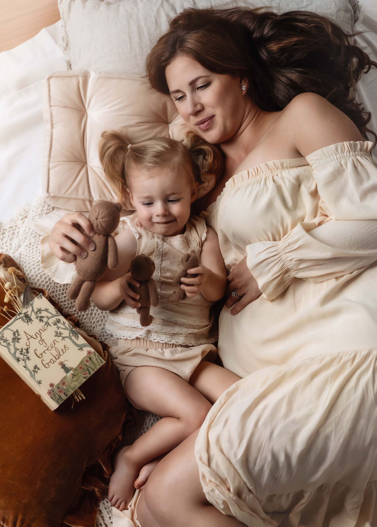 A tender family moment captured on white bedding as parent and child share story time together in soft natural light.
