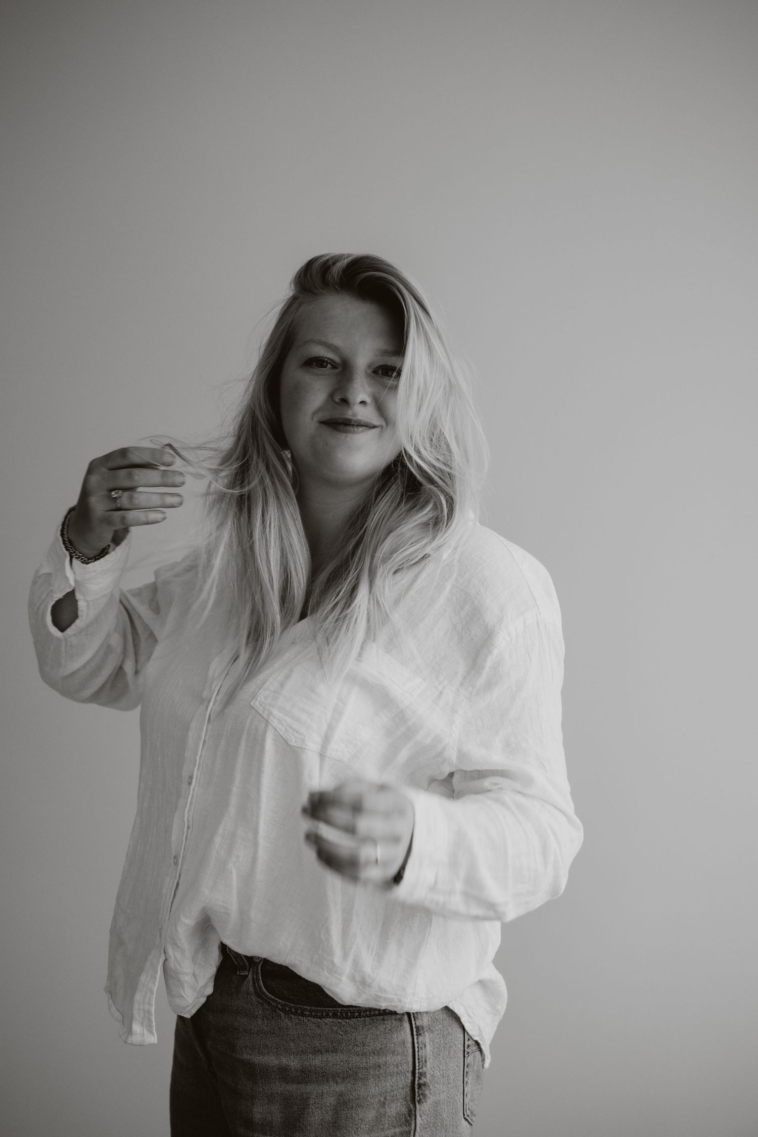 Black and white photo of a blonde woman in a white shirt and jeans gesturing with both hands.
