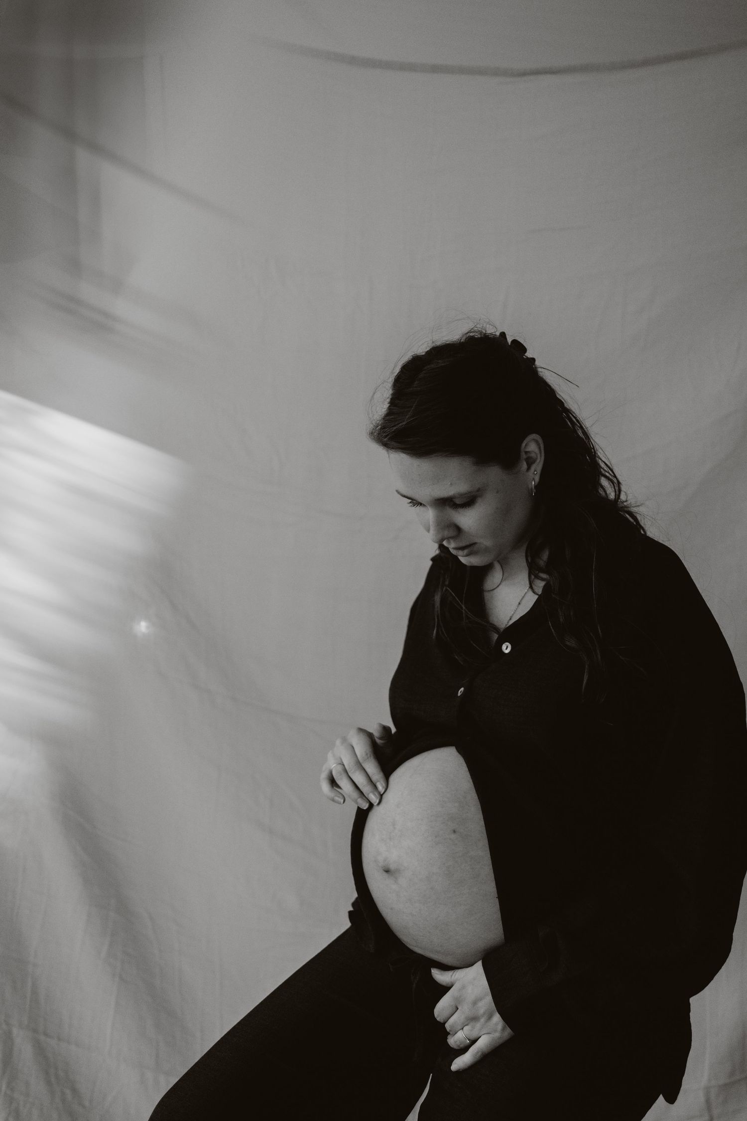 Black and white maternity photo of woman in black outfit looking down at her baby bump.
