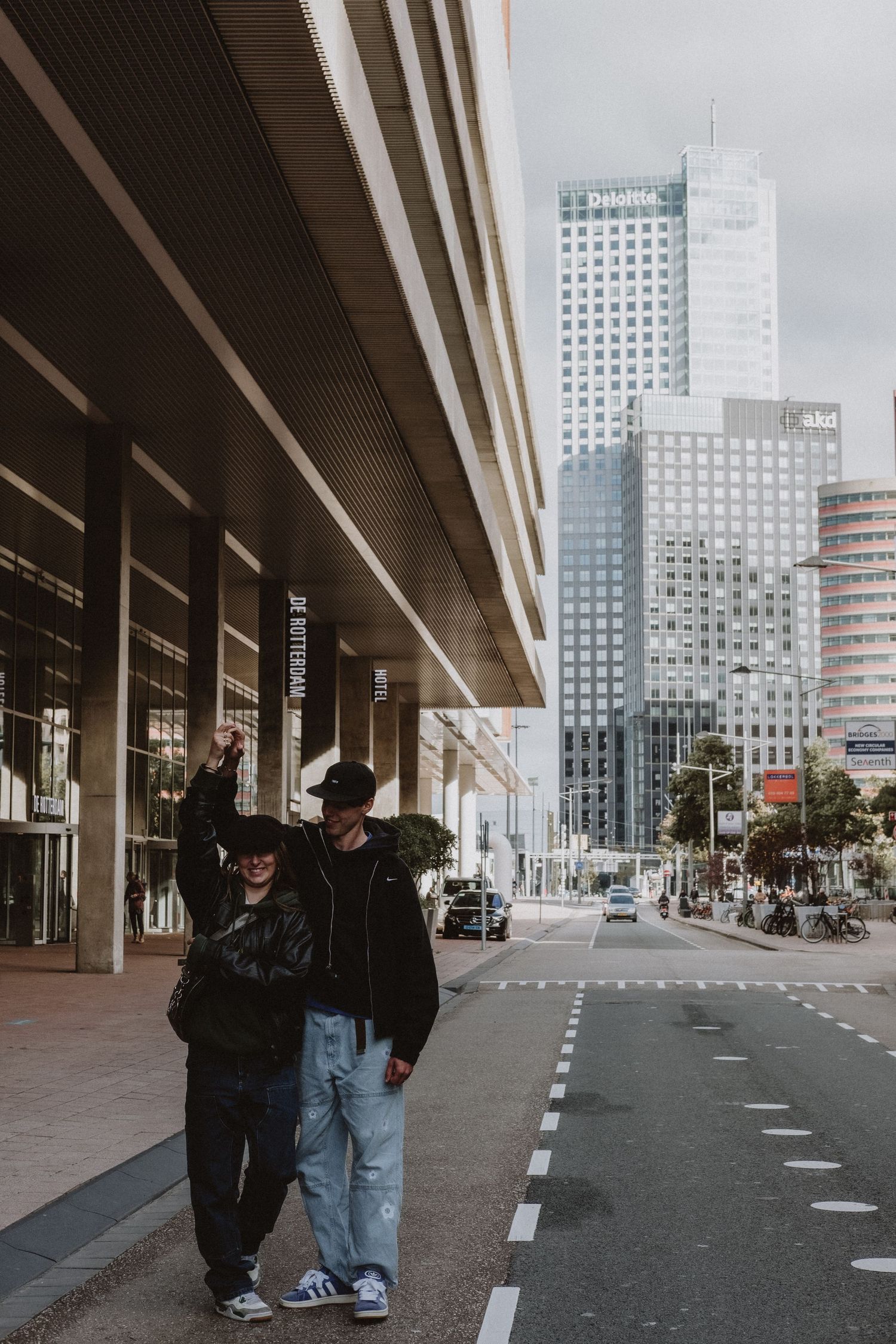 Young couple posing together on city street with tall modern skyscrapers in the background.