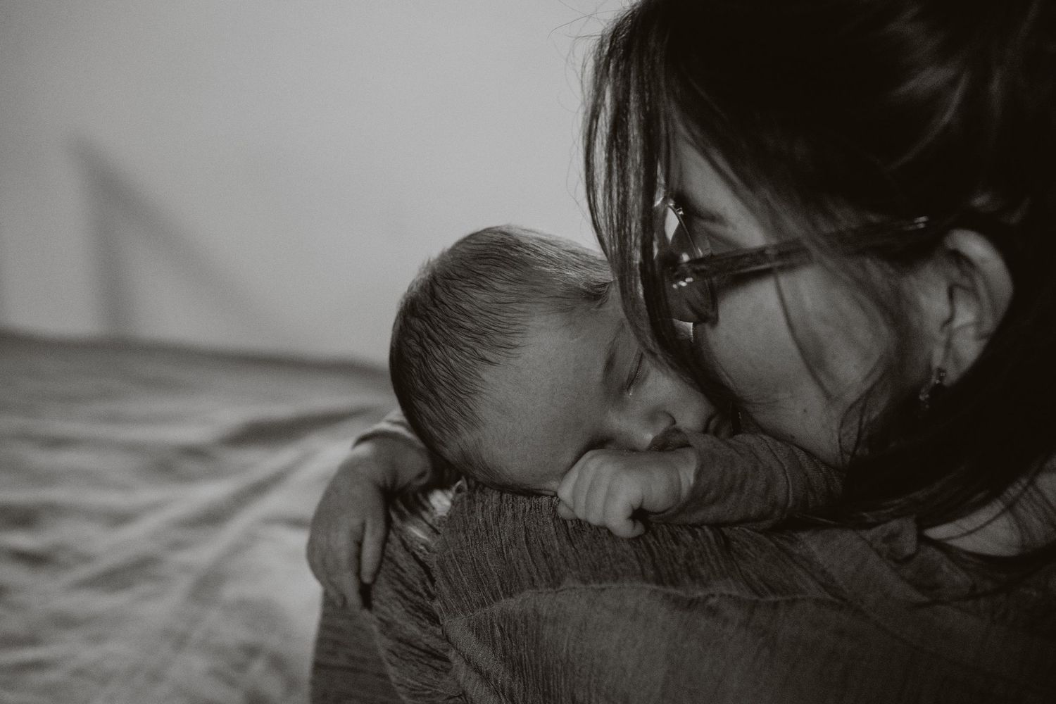 Black and white close-up of mother with glasses gently nuzzling her sleeping newborn baby.