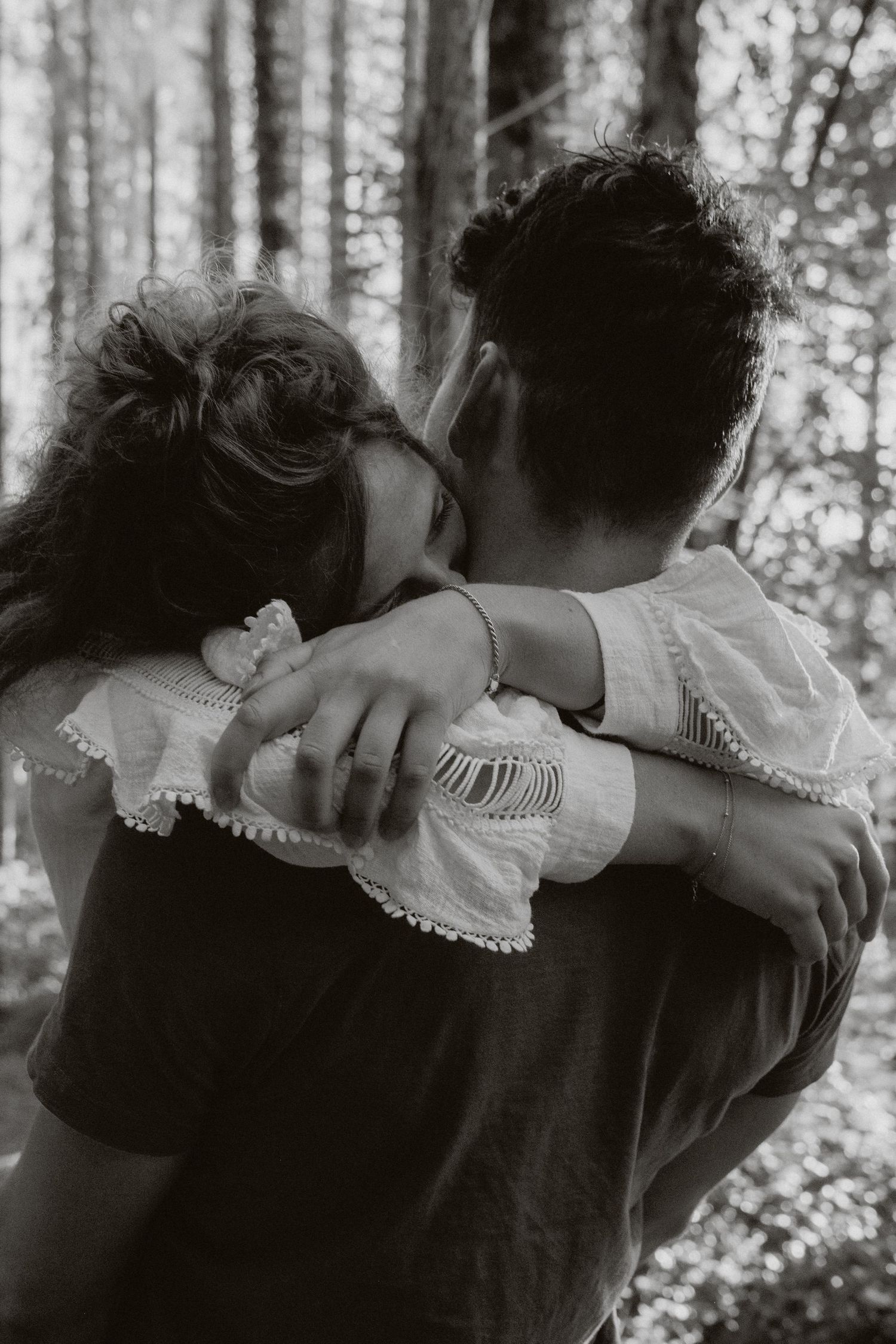 Black and white photo of couple embracing and kissing in a forest setting.
