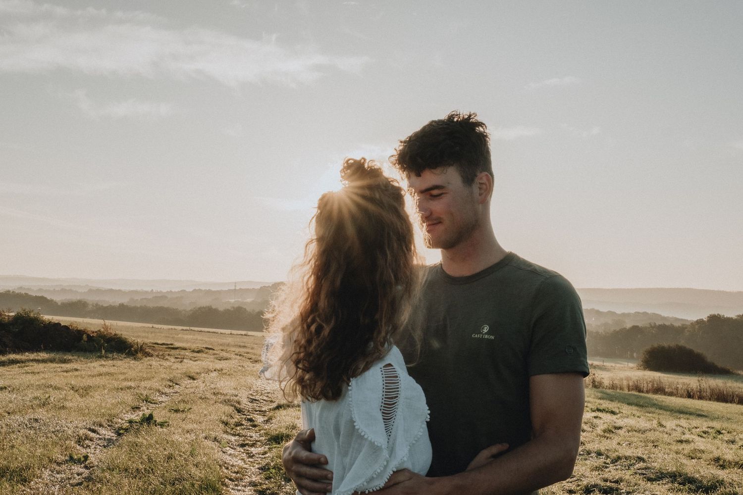 Young couple sharing romantic moment in golden sunset light in open countryside field.